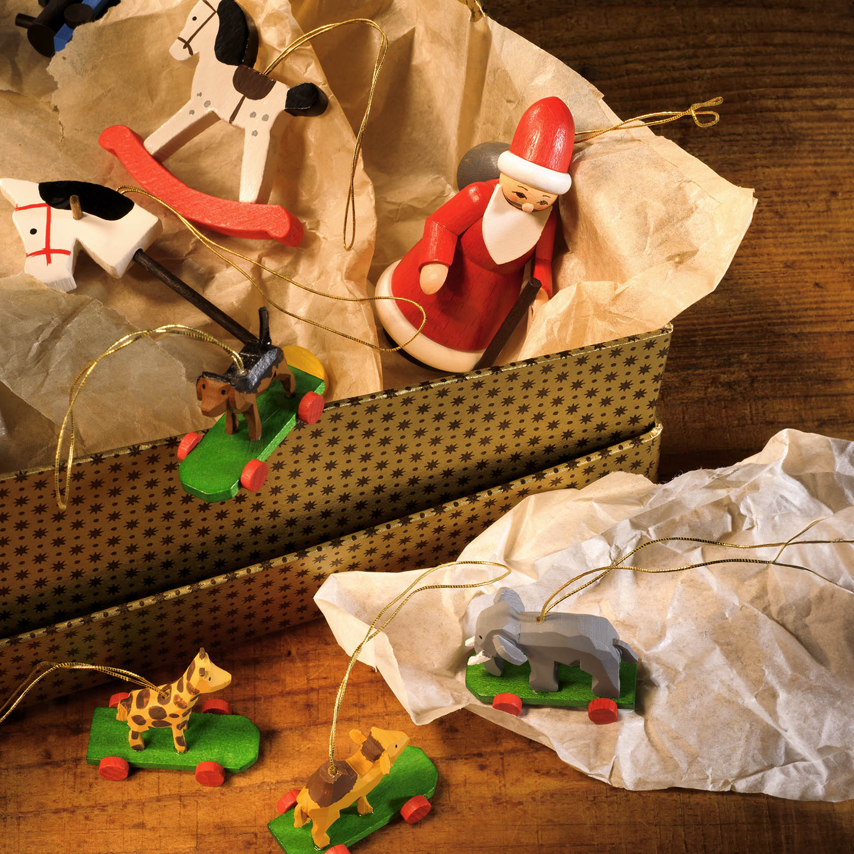 Handgeschnitzte hölzerne Weihnachtsschmuckstücke in Form von Tieren auf Rädern und einem Weihnachtsmann, die in einer Schachtel liegen.