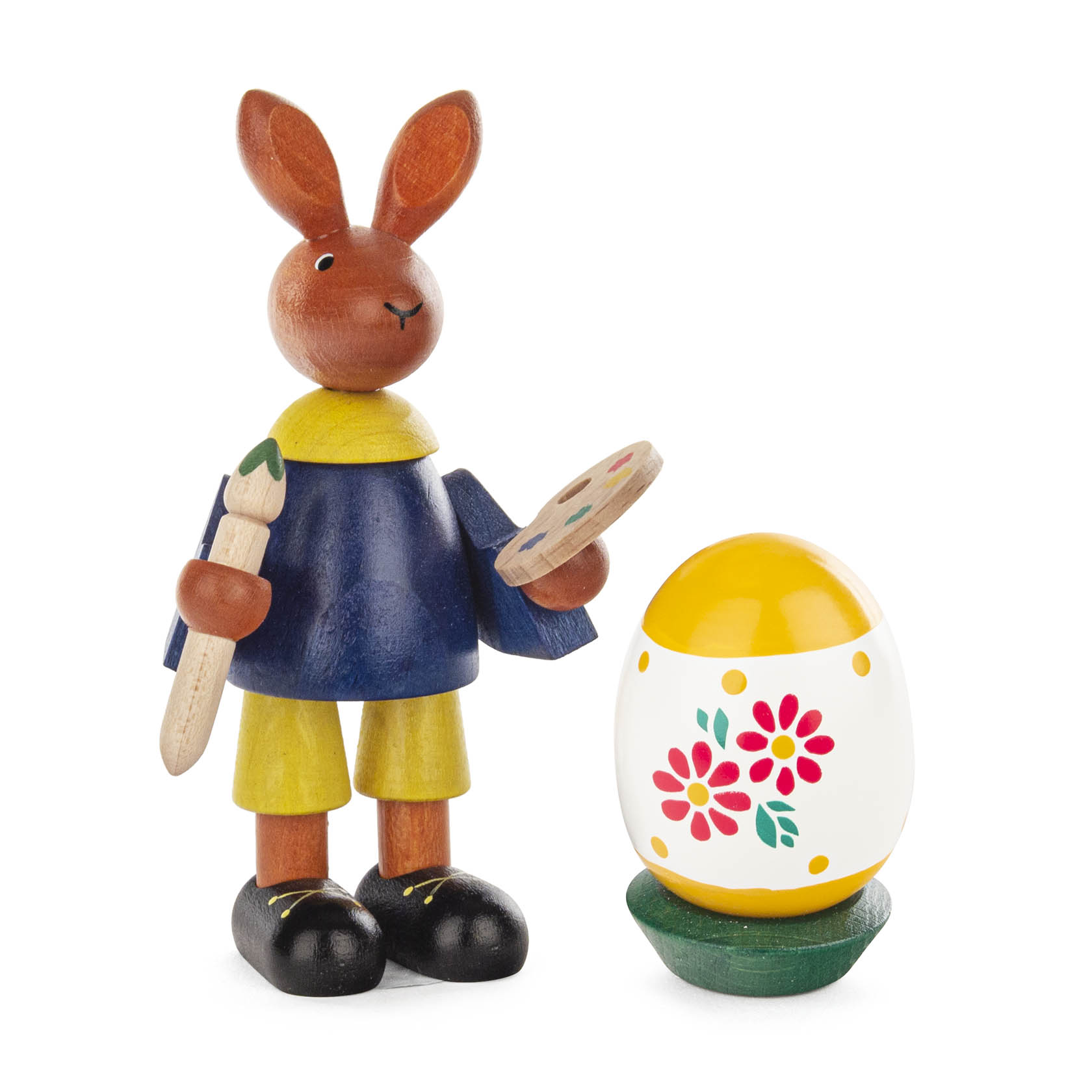 Holzfigur eines Osterhasen in gelben Hosen und blauem Oberteil, der eine Palette und Pinsel hält, neben einem dekorierten Osterei auf einem grünen Ständer. im Dregeno Online Shop günstig kaufen