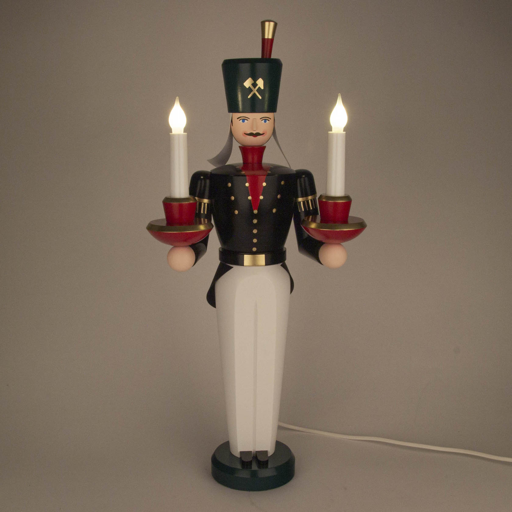 Farbig bemalter Lichterbergmann in traditioneller Bergmannsuniform. Hält in jeder Hand einen elektrischen Kerzenleuchter, leuchtet elektrisch.