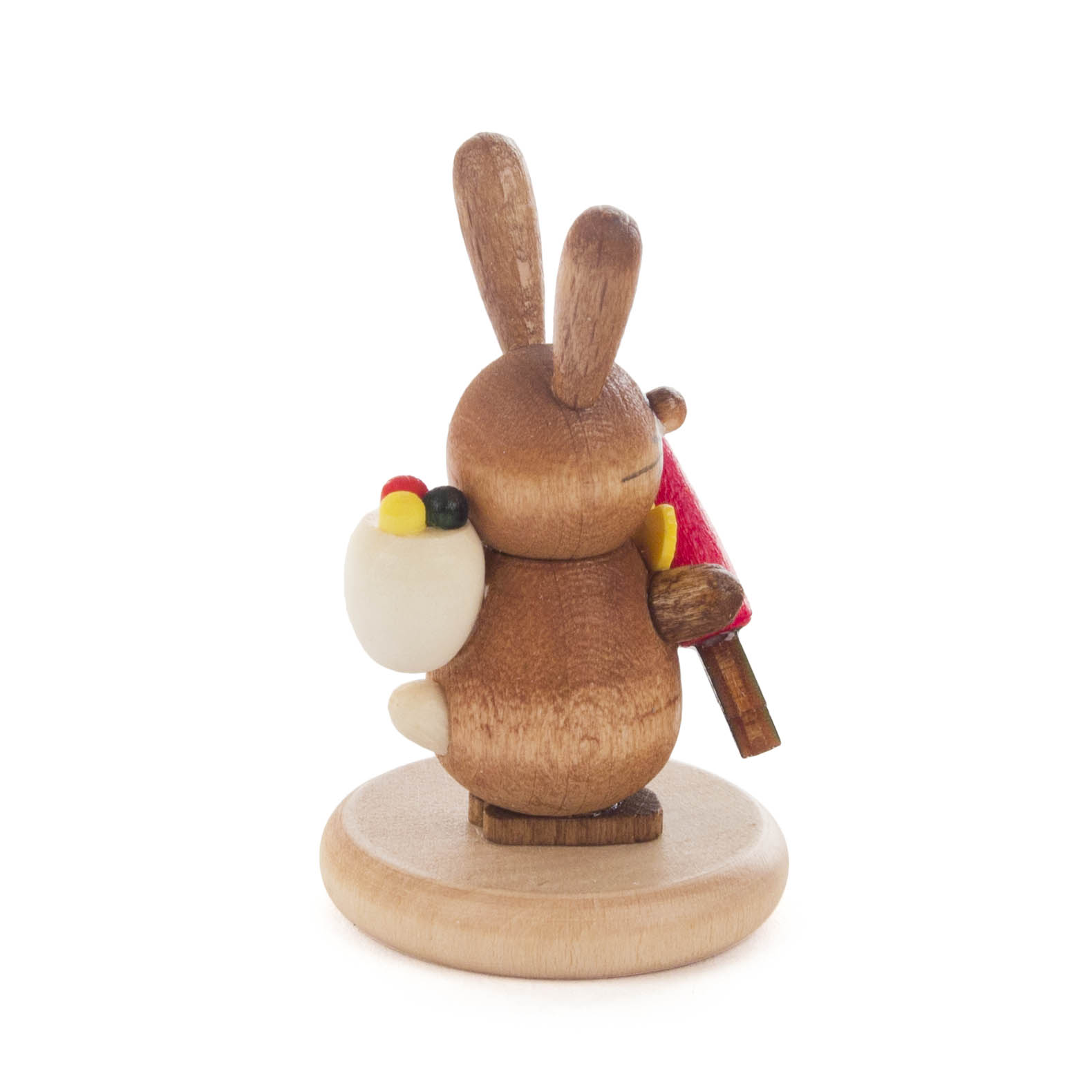 Ein lasierter, farbiger Holz-Hase steht auf einem runden Sockel und hält eine Möhre. Der Hase hat lange Ohren und einen bemalten Körper.