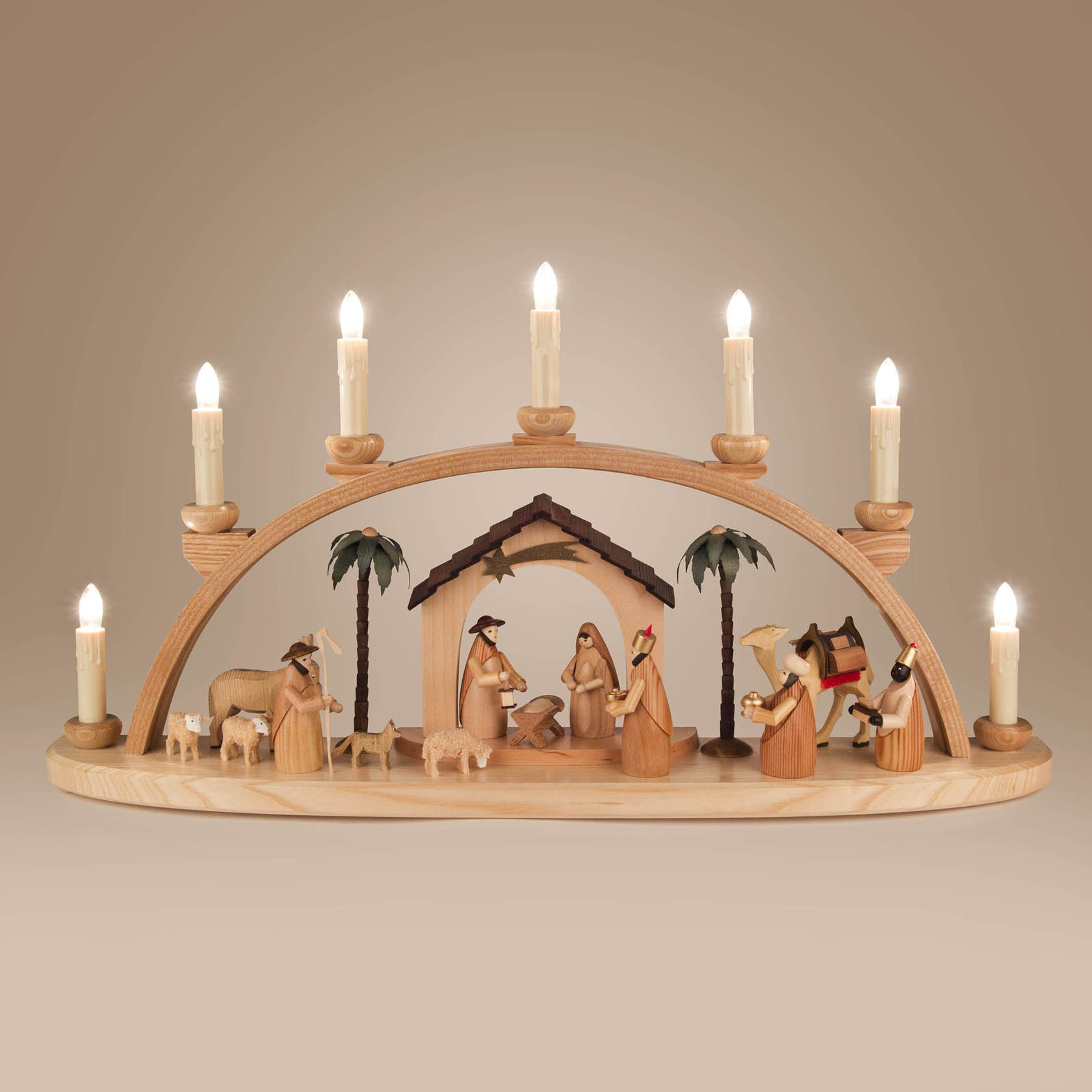 Ein traditioneller Schwibbogen aus Holz zeigt die Darstellung der Geburt Christi. Er ist mit Figuren der Heiligen Familie, Hirten, Tieren und Palmen gestaltet und elektrisch beleuchtet.