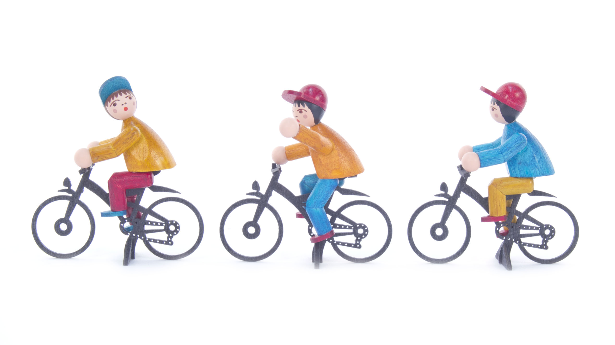Drei farbig lasierte Holzfiguren als Fahrradfahrer. Alle fahren nach rechts. Der erste trägt Rot, der zweite Gelb, der dritte Blau.