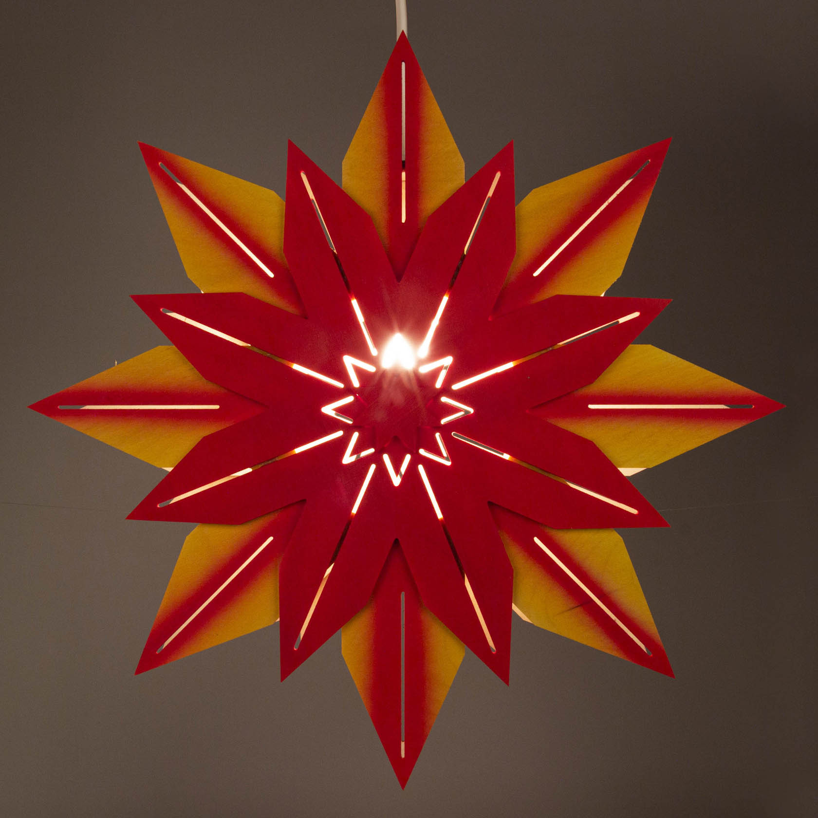 Ein gelb-roter Weihnachtsstern mit elektrischer Beleuchtung, der aus roten und gelben Papiersegmenten besteht und in der Mitte beleuchtet ist.