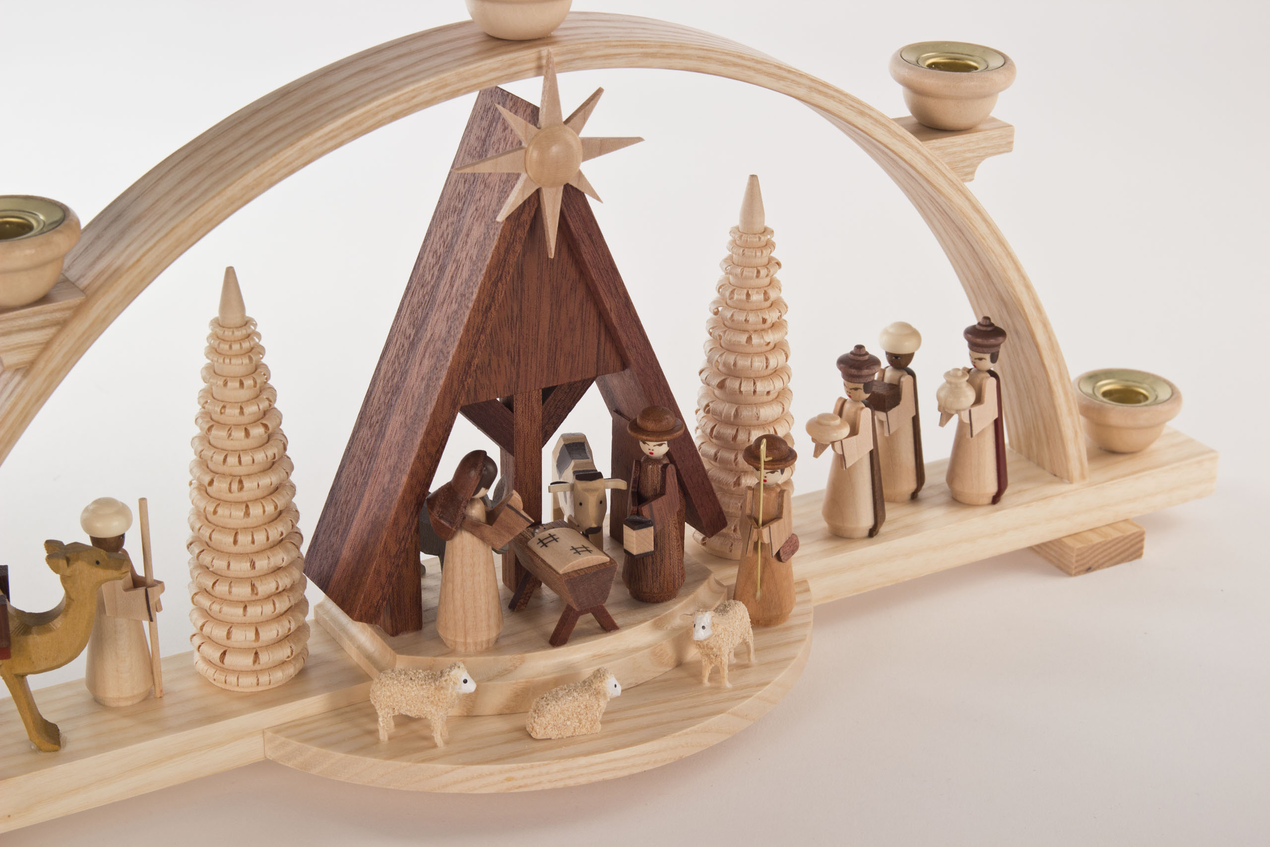 Holzschwibbogen mit Szene der Geburt Christi, Josef, Maria und Jesus in einer Krippe, umgeben von Hirten, zwei Schafen und einem Kamel, alle in natürlichen Holztönen.