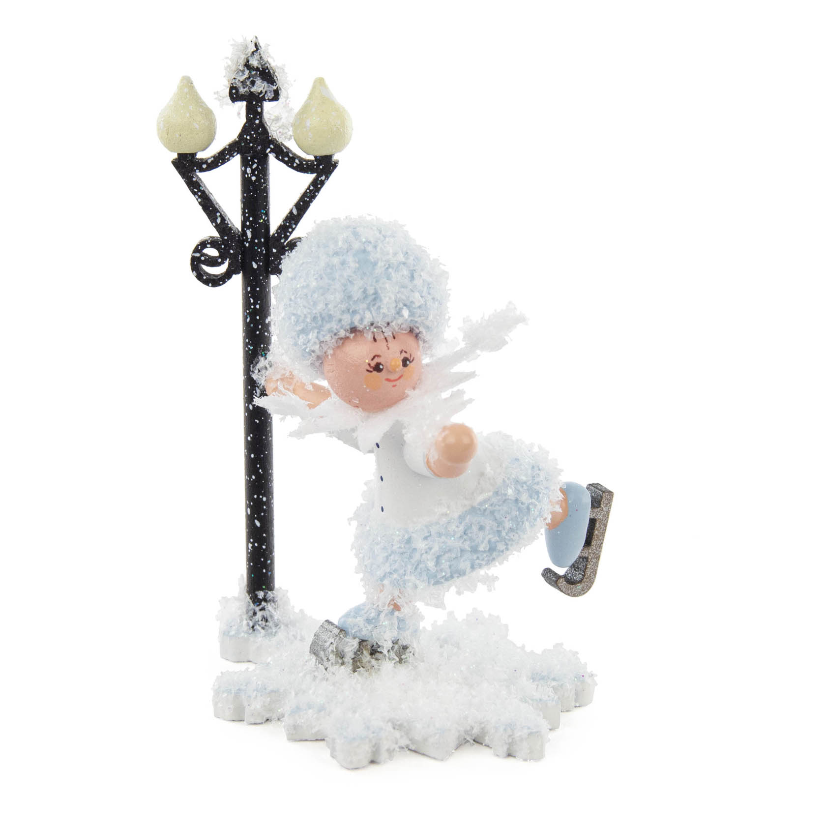 Kleine Holzfigur eines Schlittschuh fahrenden Mädchens mit flauschigem blauen Mantel und Hut. Sie gleitet auf einem Schneefeld neben einer Laterne. im Dregeno Online Shop günstig kaufen