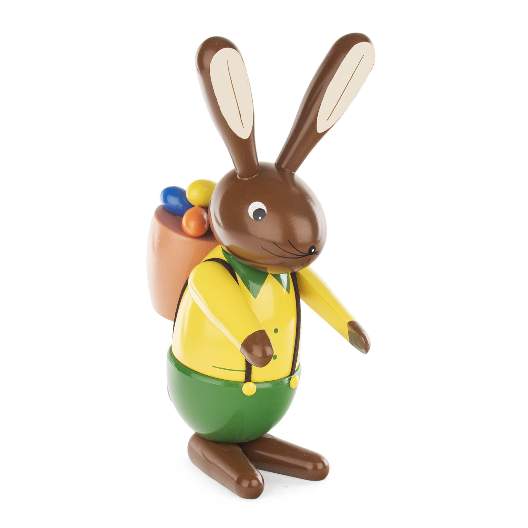 Eine mittelgroße, farbenfrohe Hasenfigur mit braunem Fell. Er trägt eine gelbe Jacke, grüne Hose und einen bunten Korb mit Eiern auf dem Rücken. im Dregeno Online Shop günstig kaufen