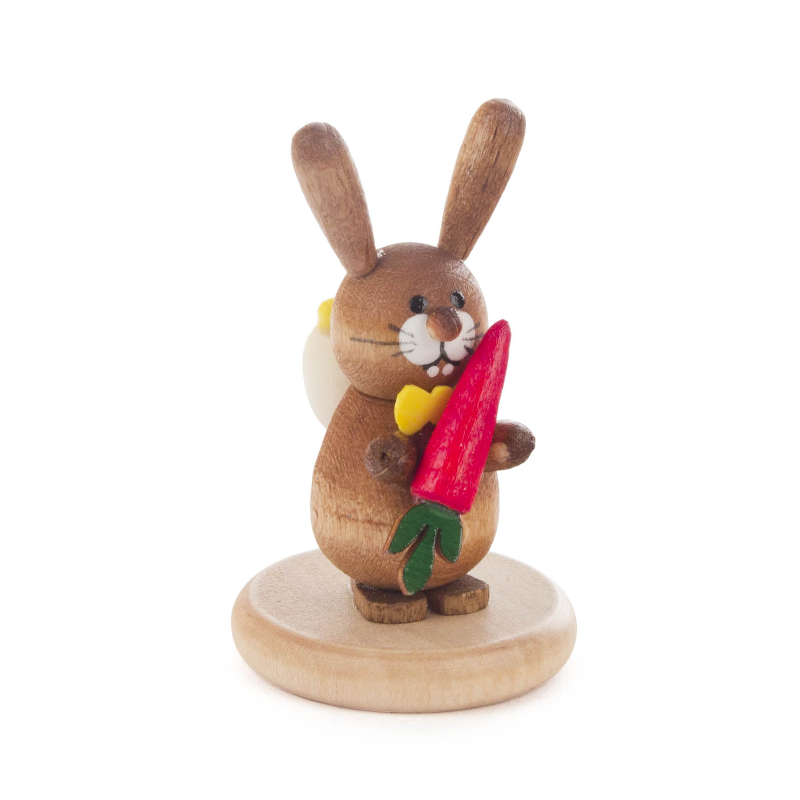 Holzfigur eines lachenden Hasen mit gelber Fliege, der eine rote Möhre hält, auf einem runden Holzsockel. im Dregeno Online Shop günstig kaufen