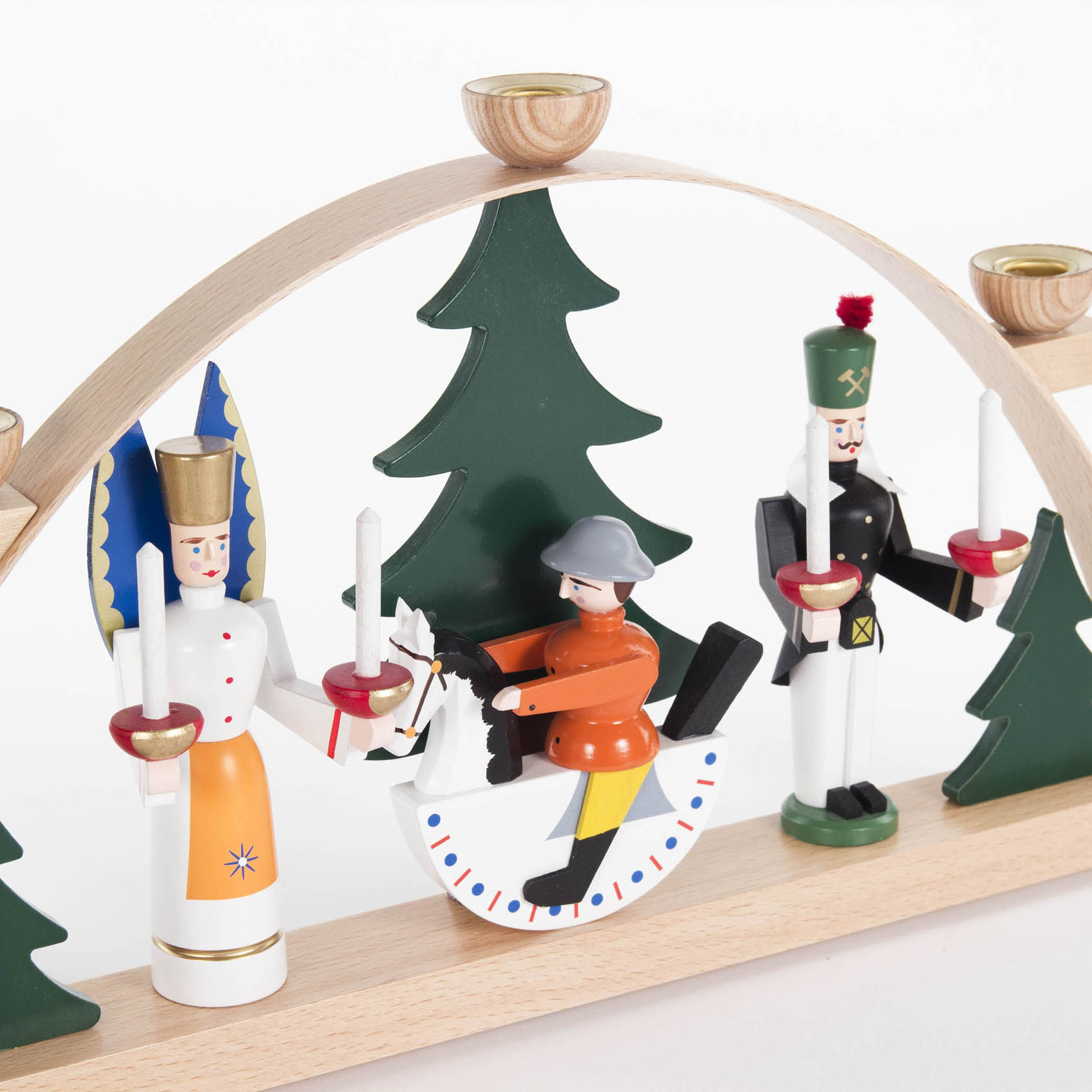 Ein farbiger Schwibbogen mit drei Figuren: einem Engel links, einem Reiter in der Mitte und einem Bergmann rechts, umgeben von grünen Tannenbäumen.