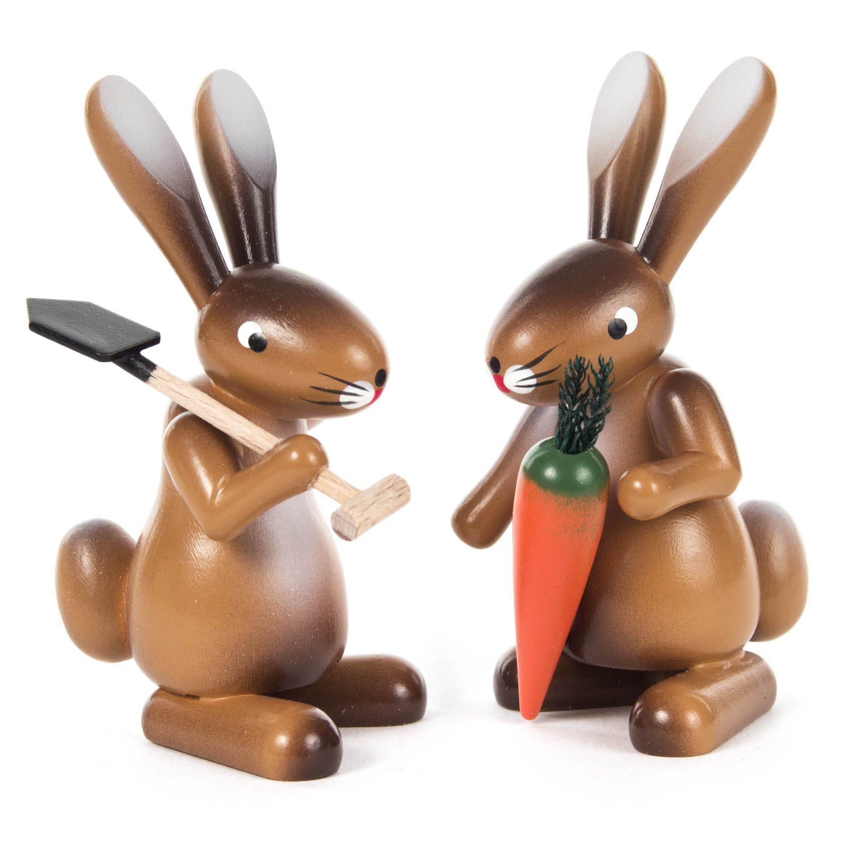 Zwei Holzhasenfiguren: Einer hält eine Karotte, der andere eine Schaufel. Beide haben aufrecht stehende Ohren und freundliche Gesichter.
