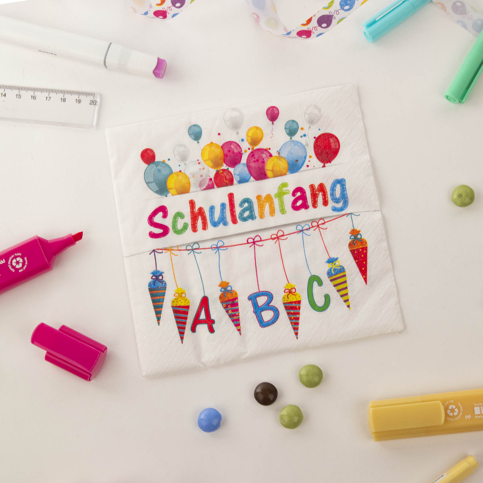 Bunte Serviette mit der Aufschrift Schulanfang, verziert mit bunten Luftballons, Zuckertüten und ABC-Buchstaben.