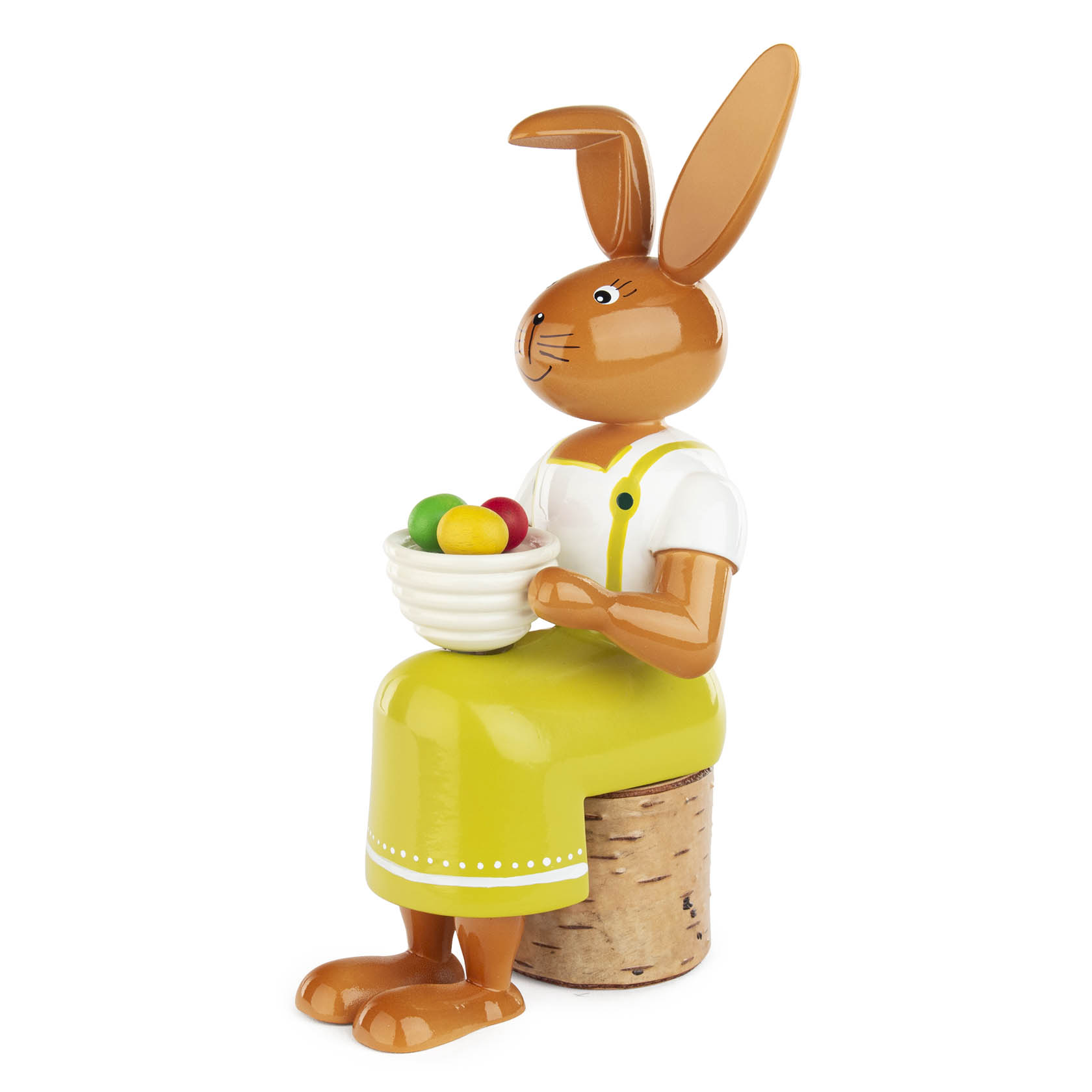 Holzfigur einer Hasenfrau mit langen Ohren, die in einem grünen Rock und Latzträger ein weißes Schüsselchen mit bunten Ostereiern hält.