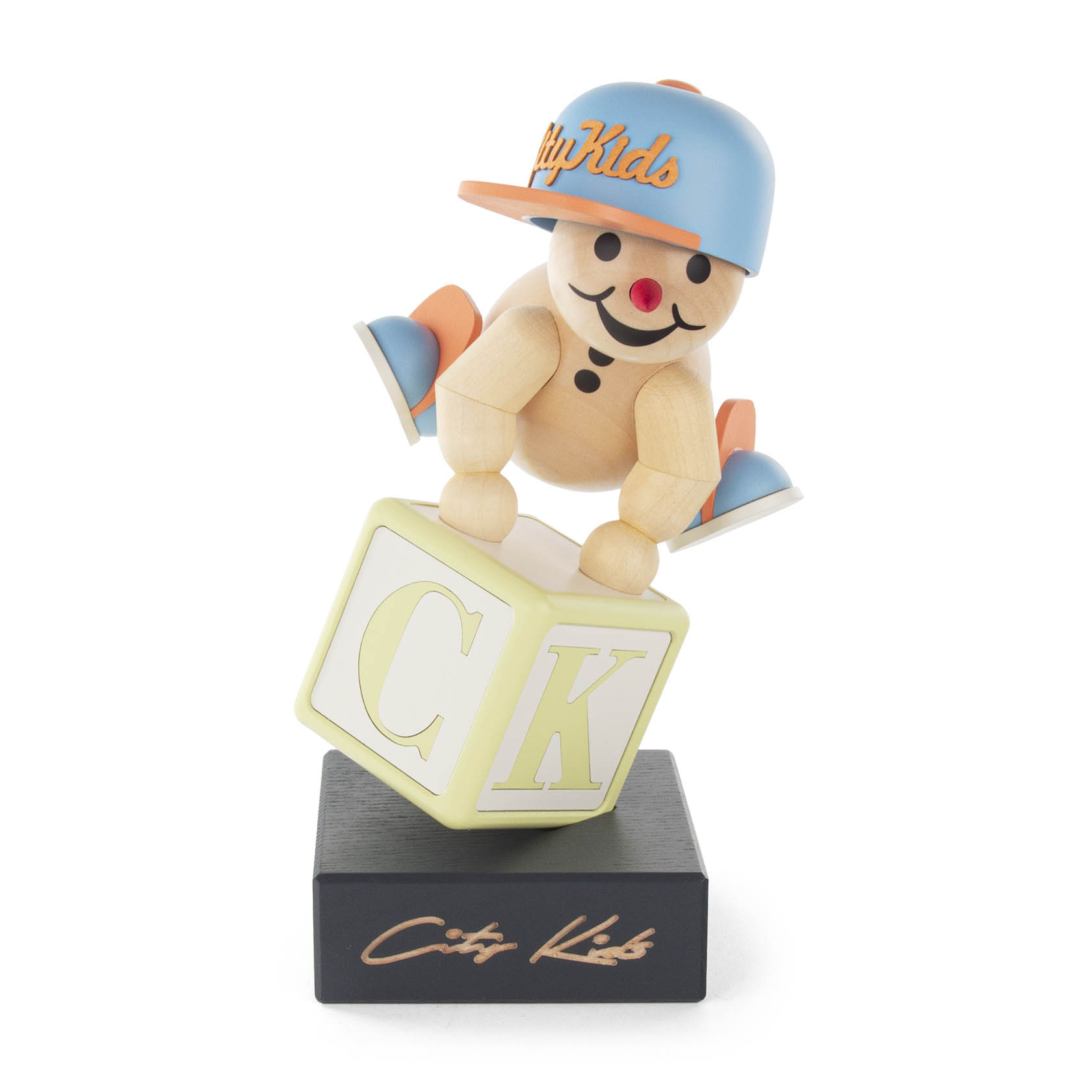 Holzfigur eines Kindes mit Baseballkappe, das auf einem Würfel mit den Buchstaben C und K balanciert. Die Base hat die Aufschrift 'City Kids'. im Dregeno Online Shop günstig kaufen
