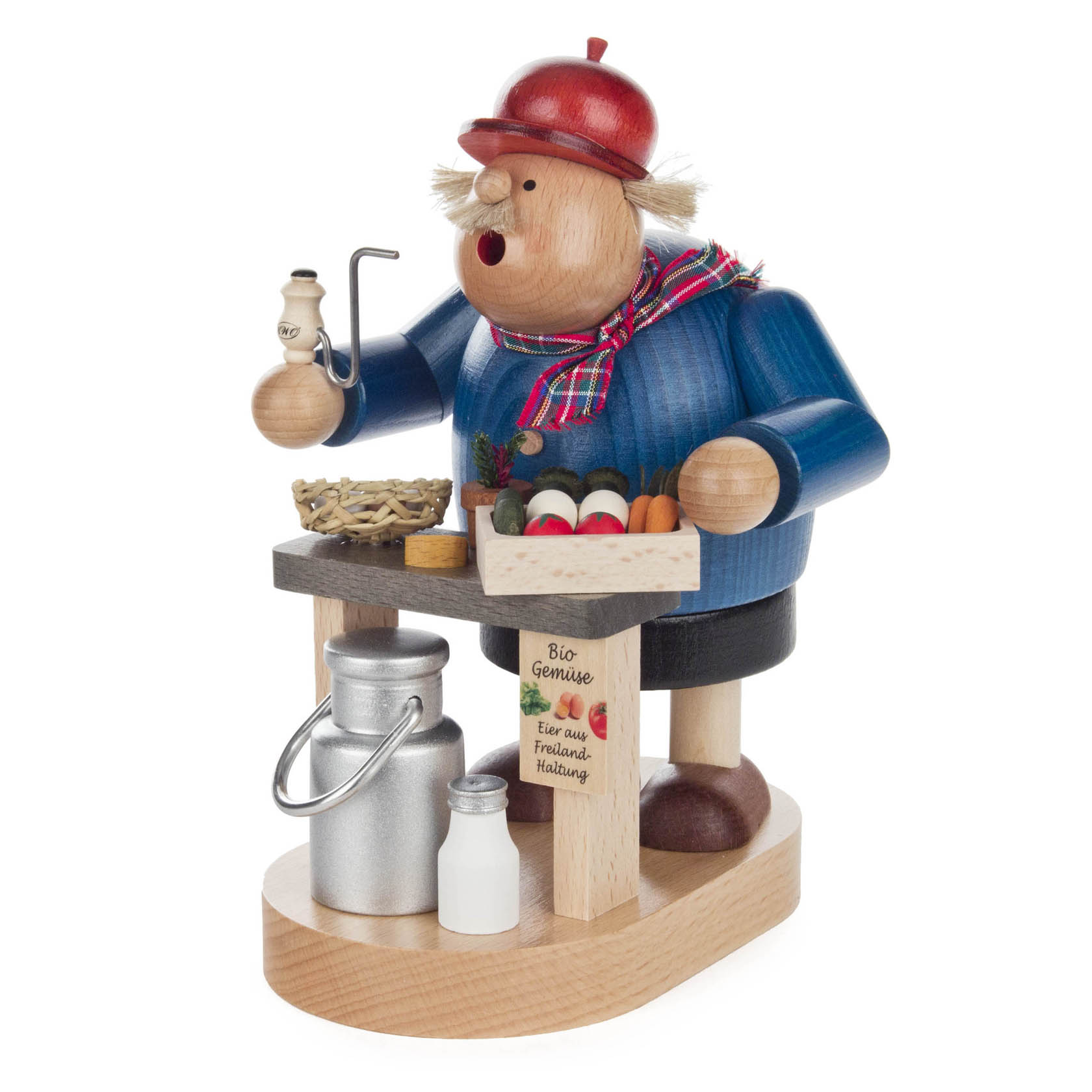 Ein 20 cm hoher Räuchermann in Form eines Bio-Bauern, der eine Pfeife raucht. Er trägt eine rote Mütze und einen blauen Pullover. Vor ihm steht ein Tisch mit Gemüse und Milchflaschen. im Dregeno Online Shop günstig kaufen