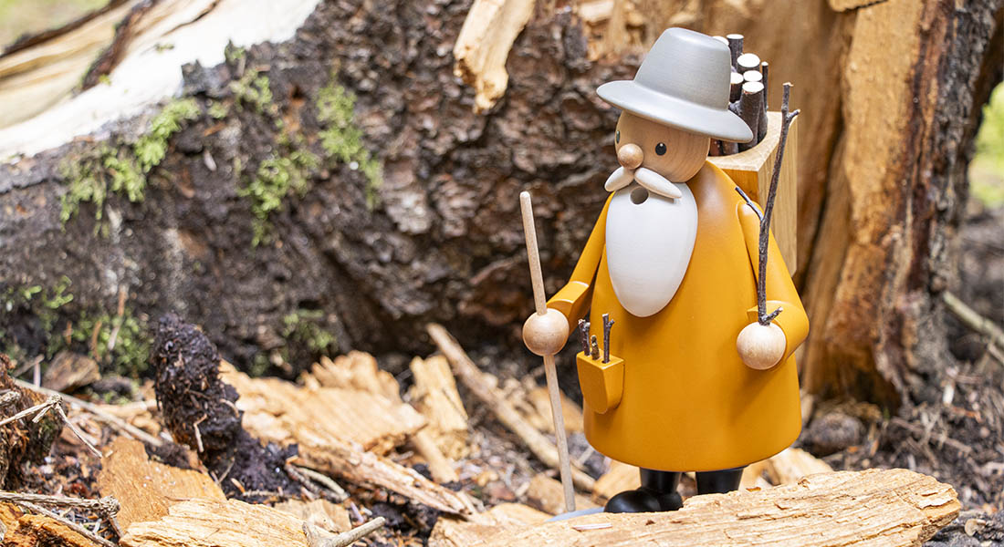 Räuchermann Holzsammler aus Holz mit Reisigbündel und Wanderstock steht vor einem alten Baumstumpf