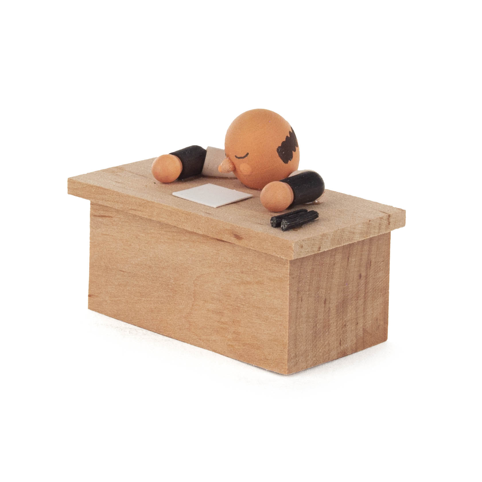 Minimalistische Figur aus Holz, die mit gesenktem Kopf und geschlossenen Augen auf einem Holztisch liegt. Neben der Figur liegen ein Stift und ein Blatt Papier.