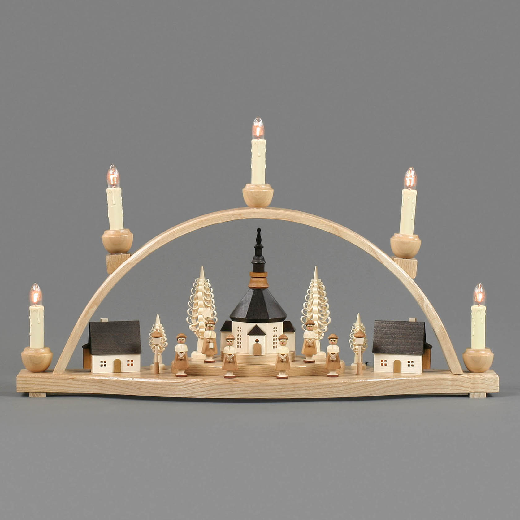 Ein Schwibbogen mit einer Darstellung des Seiffener Dorfs. In der Mitte steht eine große Kirche, umgeben von kleineren, beleuchteten Gebäuden und Kurrendesängern.
