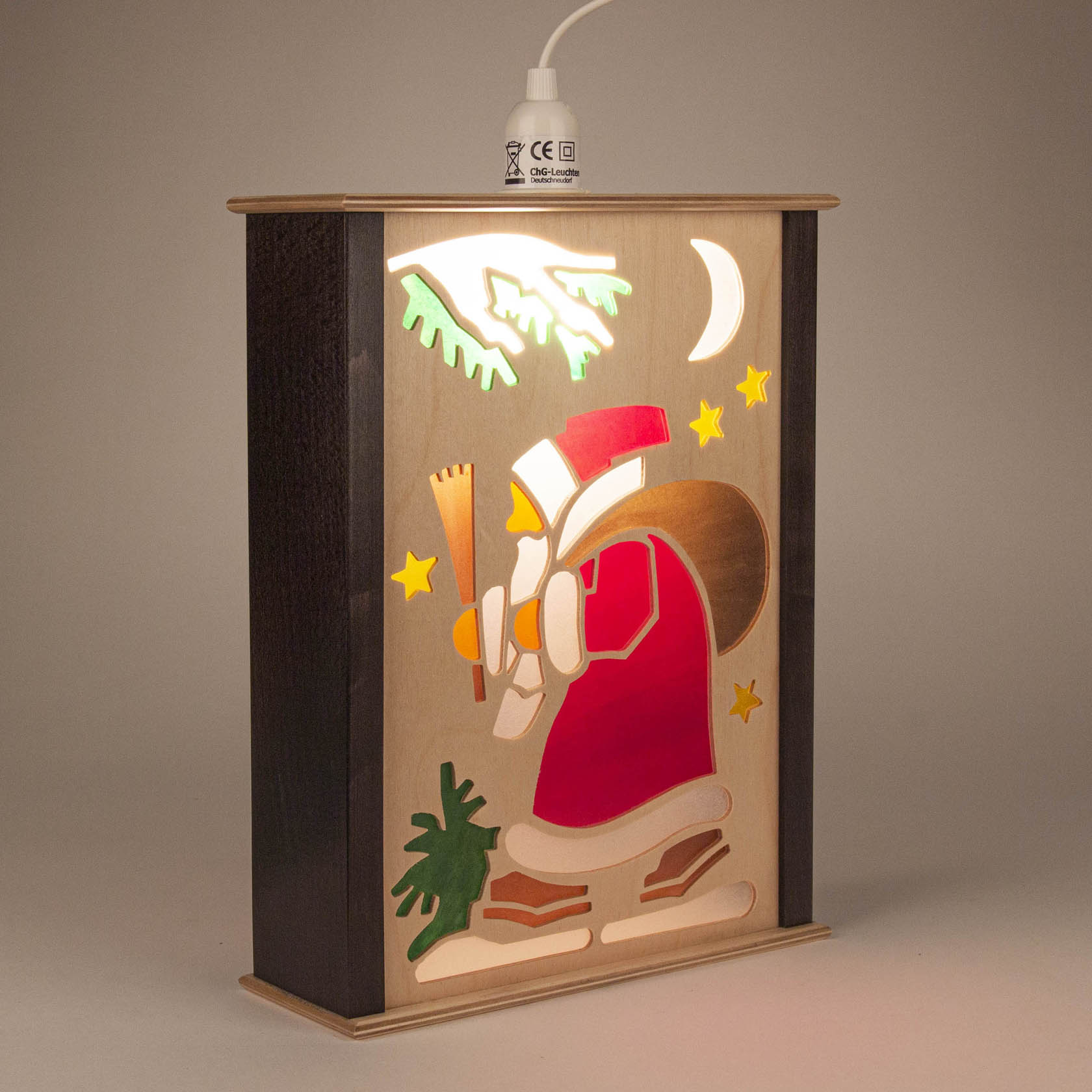 Fensterlaterne mit Holzrahmen, zeigt Weihnachtsmann mit Laterne, Mond und Sterne im Hintergrund, warme Beleuchtung aus dem Inneren.