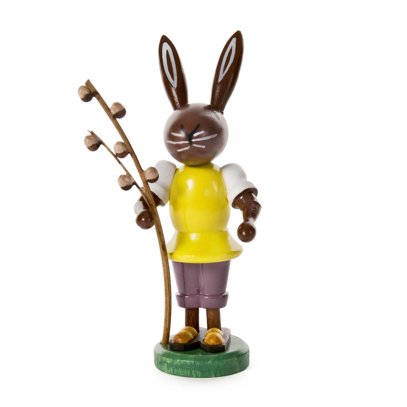 Holzfigur eines Hasen, gekleidet in gelbem Oberteil und lila Hose, hält einen Zweig mit Weidenkätzchen. im Dregeno Online Shop günstig kaufen