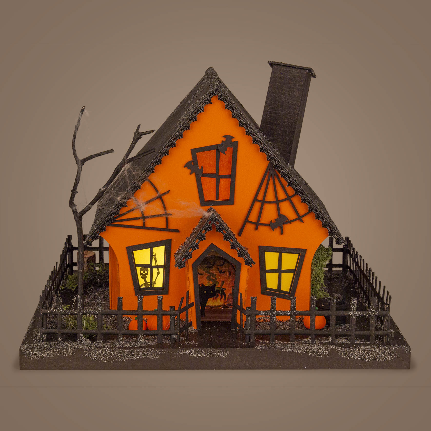 Modell eines orangefarbenen Hauses in Form eines Kürbisses mit leuchtenden Fenstern, einem schiefen Schornstein und einem kahlen Baum im Vorgarten.