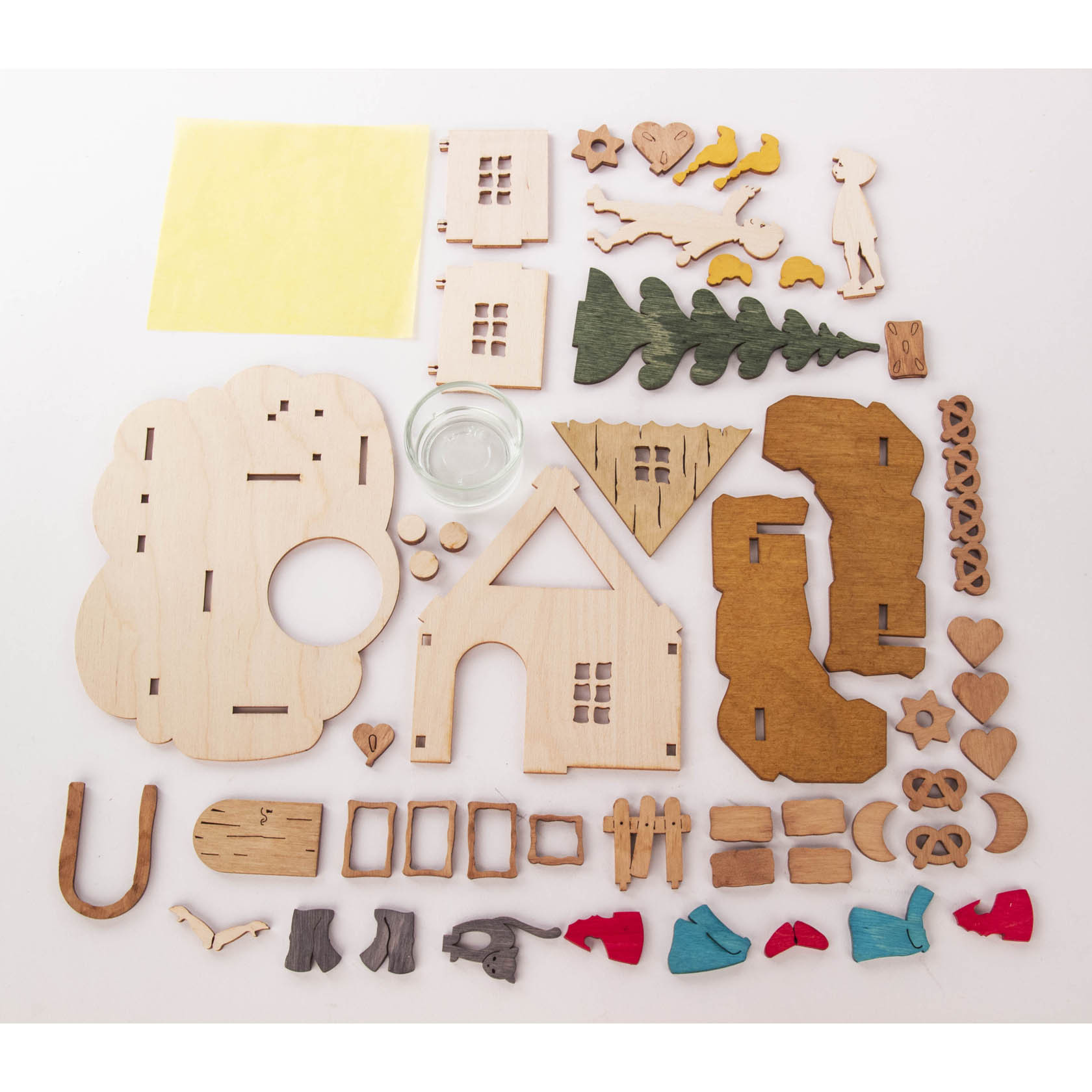 Components of a DIY tealight holder set inspired by Hansel and Gretel, including wooden shapes of a house, trees, and characters, a glass holder, and various painted pieces.