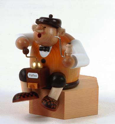 A wooden smoker figure, the 'Kaffeesachse', sits atop a block, holding a coffee mill and cup, wearing a flat cap, vest, bow tie, and checkered shoes. im Dregeno Online Shop günstig kaufen