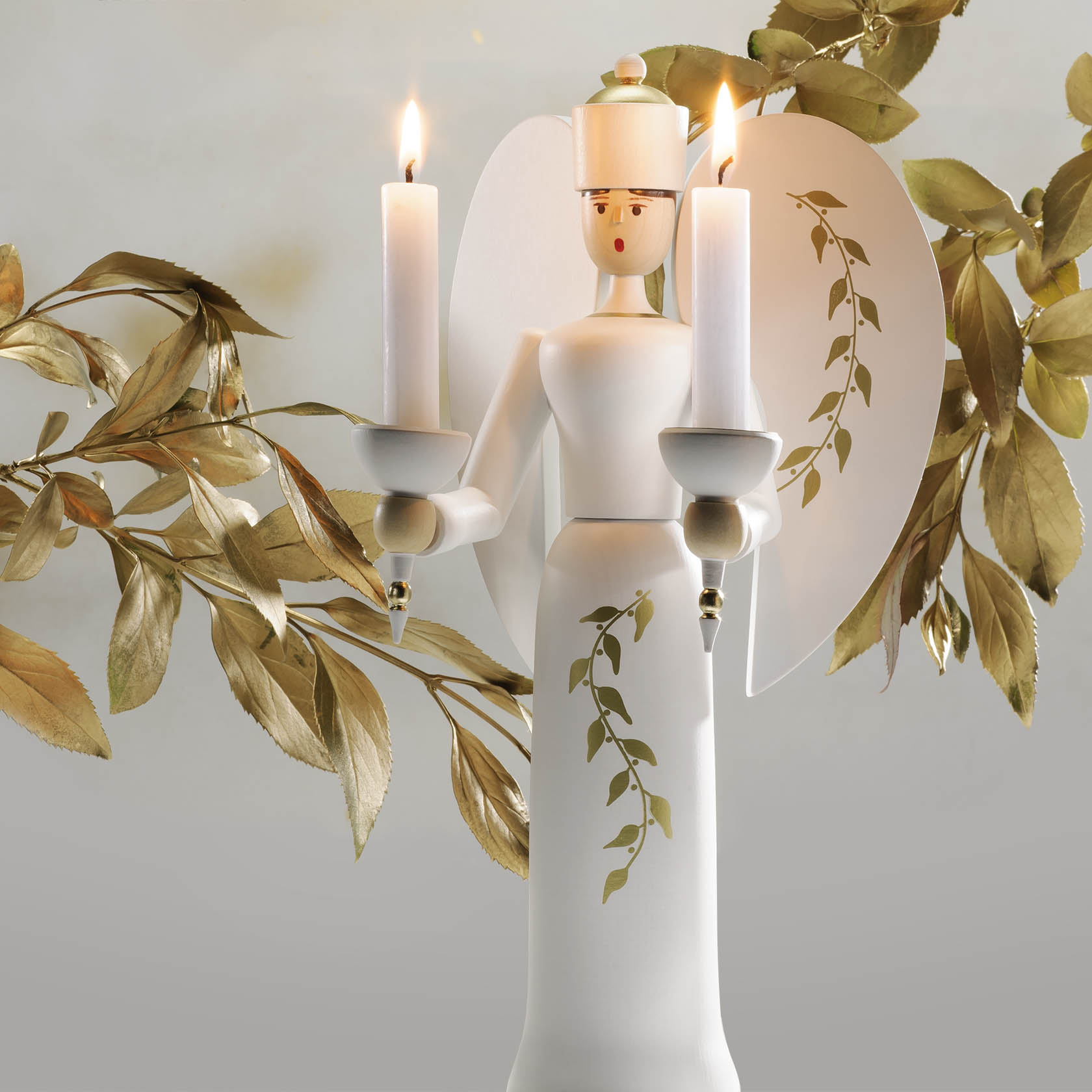 A white and gold angel figure holding two lit candles, decorated with a floral pattern on its robe and wings.