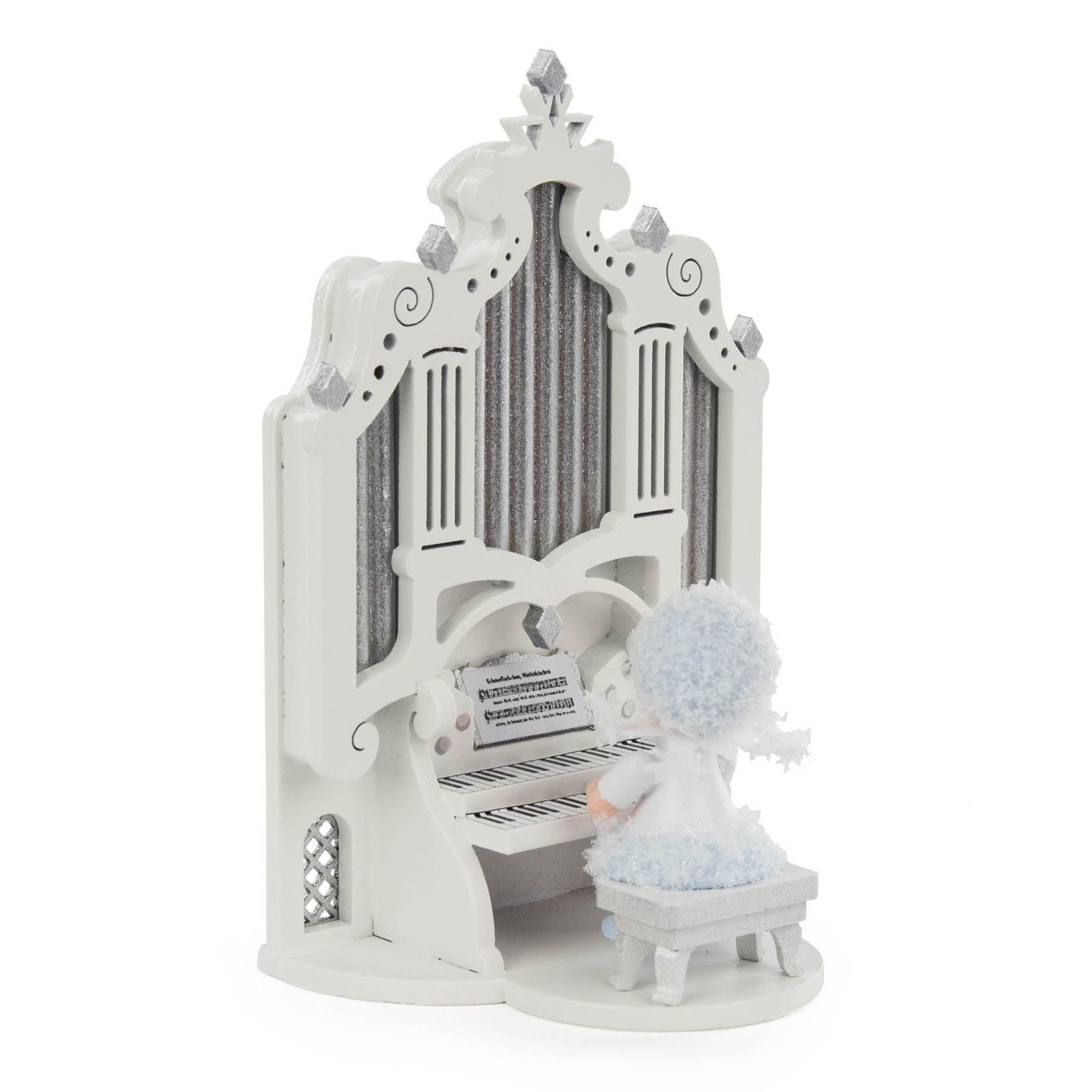 Eine Figur eines Mädchens, das als Schneeflöckchen verkleidet ist, sitzt auf einem Hocker vor einer weißen, verzierten Orgel.