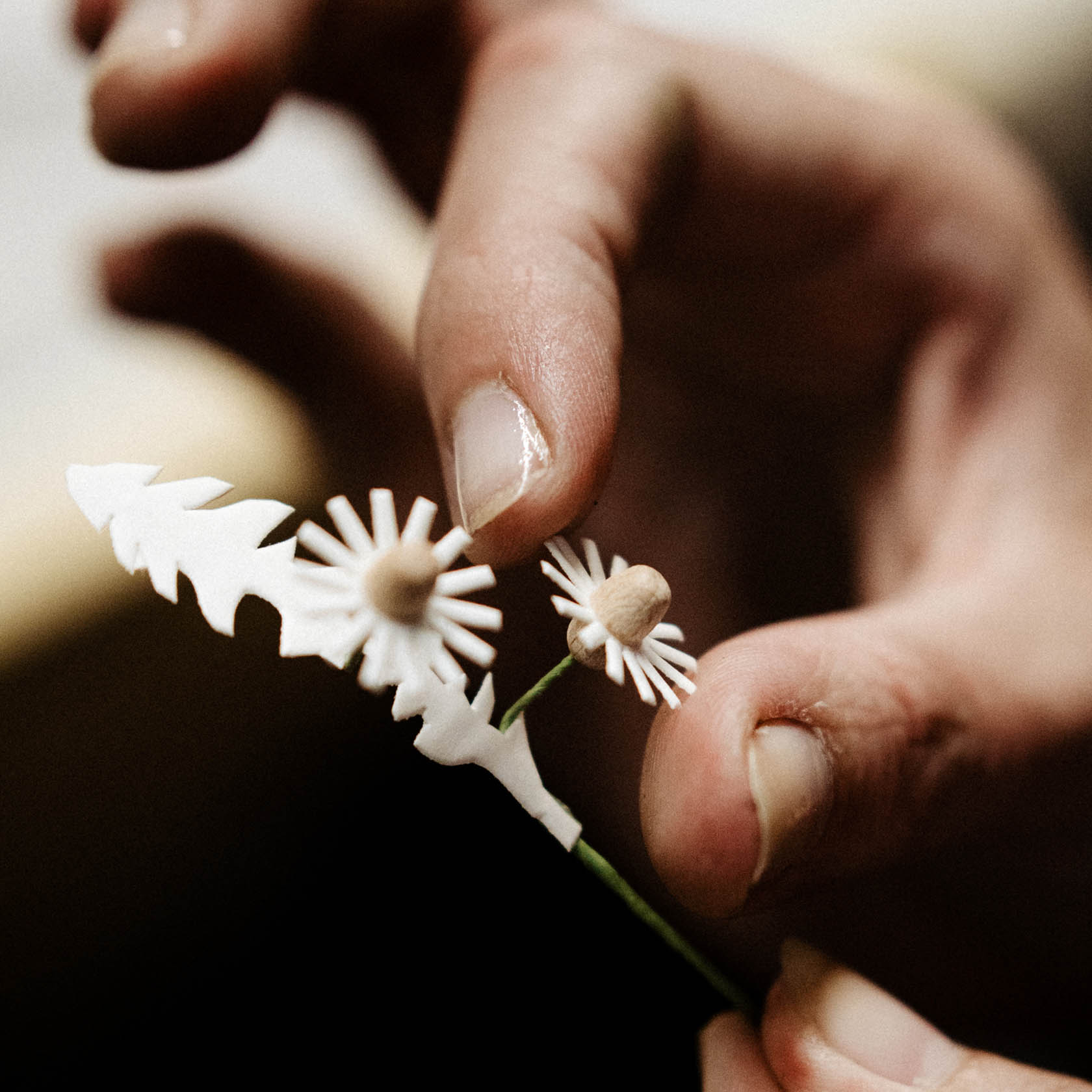 Close-up of two hands delicately holding a small handmade paper flower resembling a dandelion.