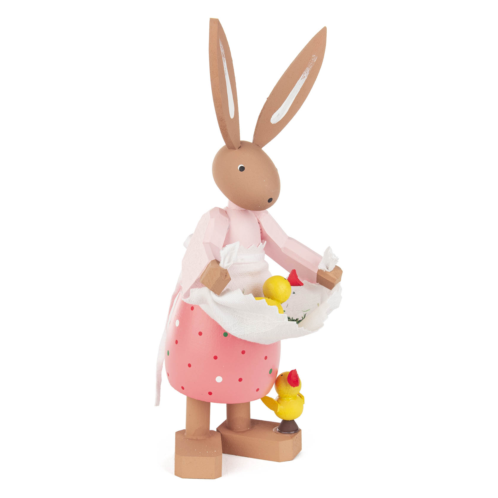 Holzfigur Osterhase Hanni in rosa Schürze, hält ein weißes Tuch mit gelbem Küken darin, daneben steht ein weiteres Küken auf dem Boden.