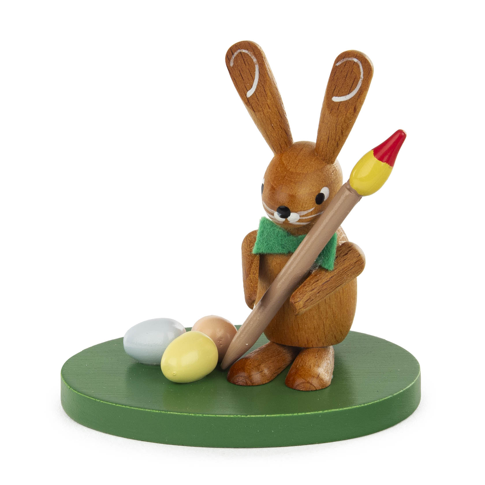 Holzhase mit grünem Schal hält einen großen Pinsel und steht neben zwei bemalten Eiern auf grünem Untergrund. im Dregeno Online Shop günstig kaufen