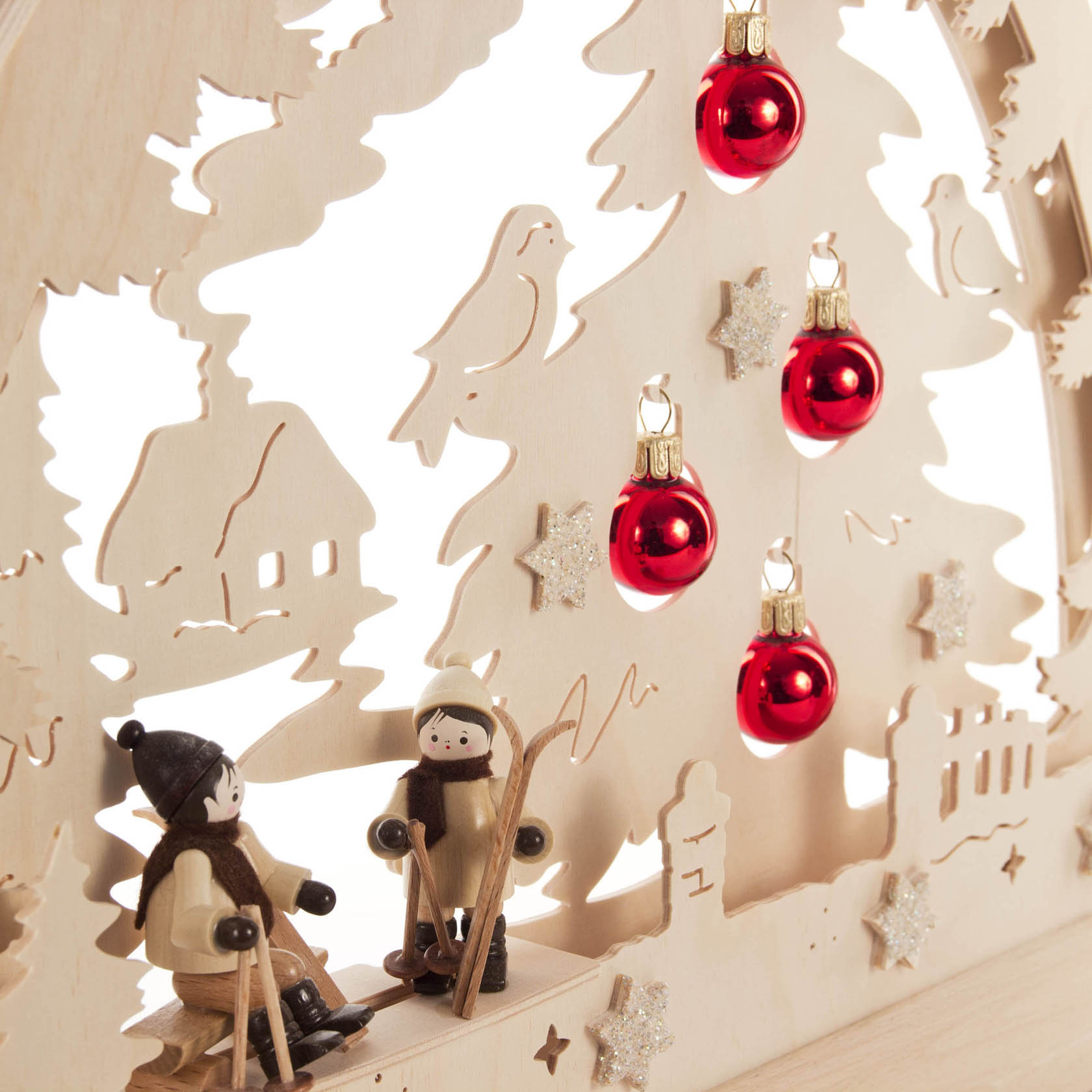 Holzrundbogen mit Skifahrerfiguren, rotem Weihnachtsbaumschmuck und LED-Bandbeleuchtung, verziert mit Weihnachtsbaum und sowie einem Vogel und Häusern im Hintergrund.