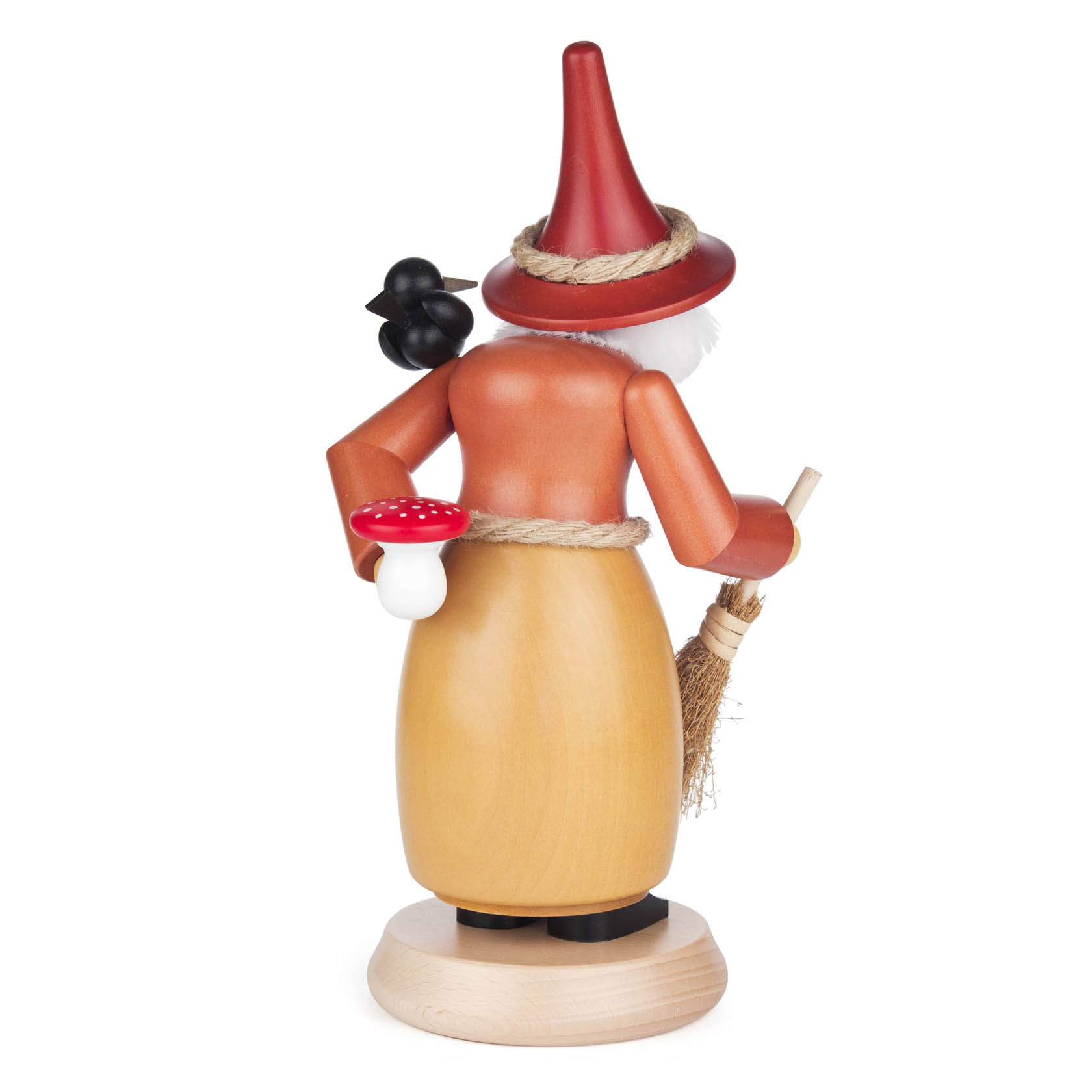 A wooden smoking witch figurine with a red hat and orange dress, holding a broomstick and a small red mushroom in her hand.