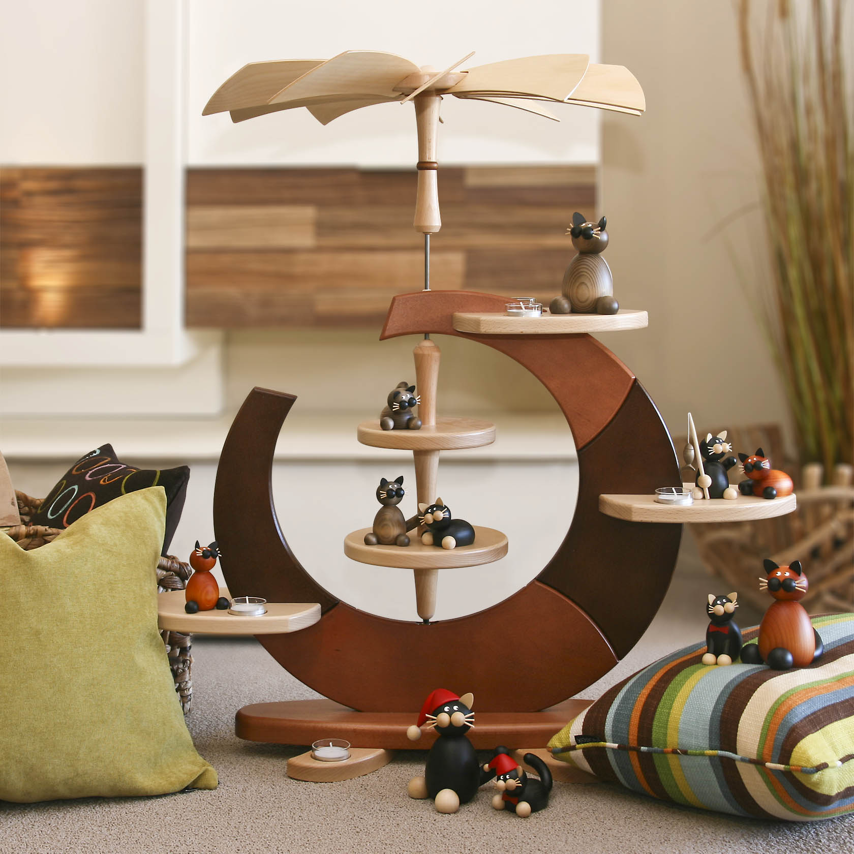 Eine dekorative Holzpyramide in Form eines offenen Kreises, bestehend aus mehreren Ebenen, geeignet für Teelichte. Verschiedene kleine Holzfiguren, hauptsächlich Katzen, sind darauf platziert.