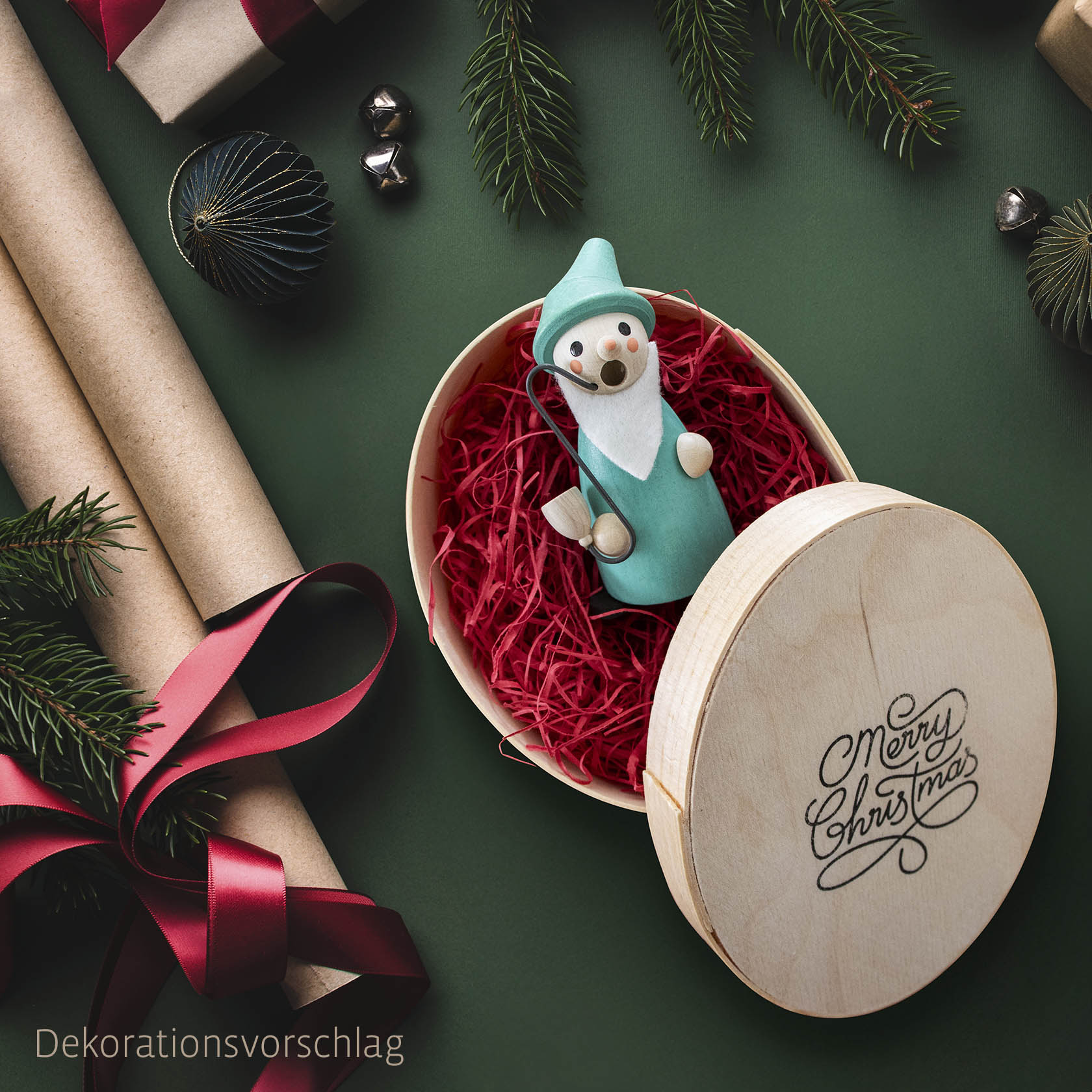 Mini-Räuchermännchen Wichtel in blauer Kleidung sitzt in einer offenen Spandose mit 'Merry Christmas' Motiv, umgeben von rotem Füllmaterial. im Dregeno Online Shop günstig kaufen