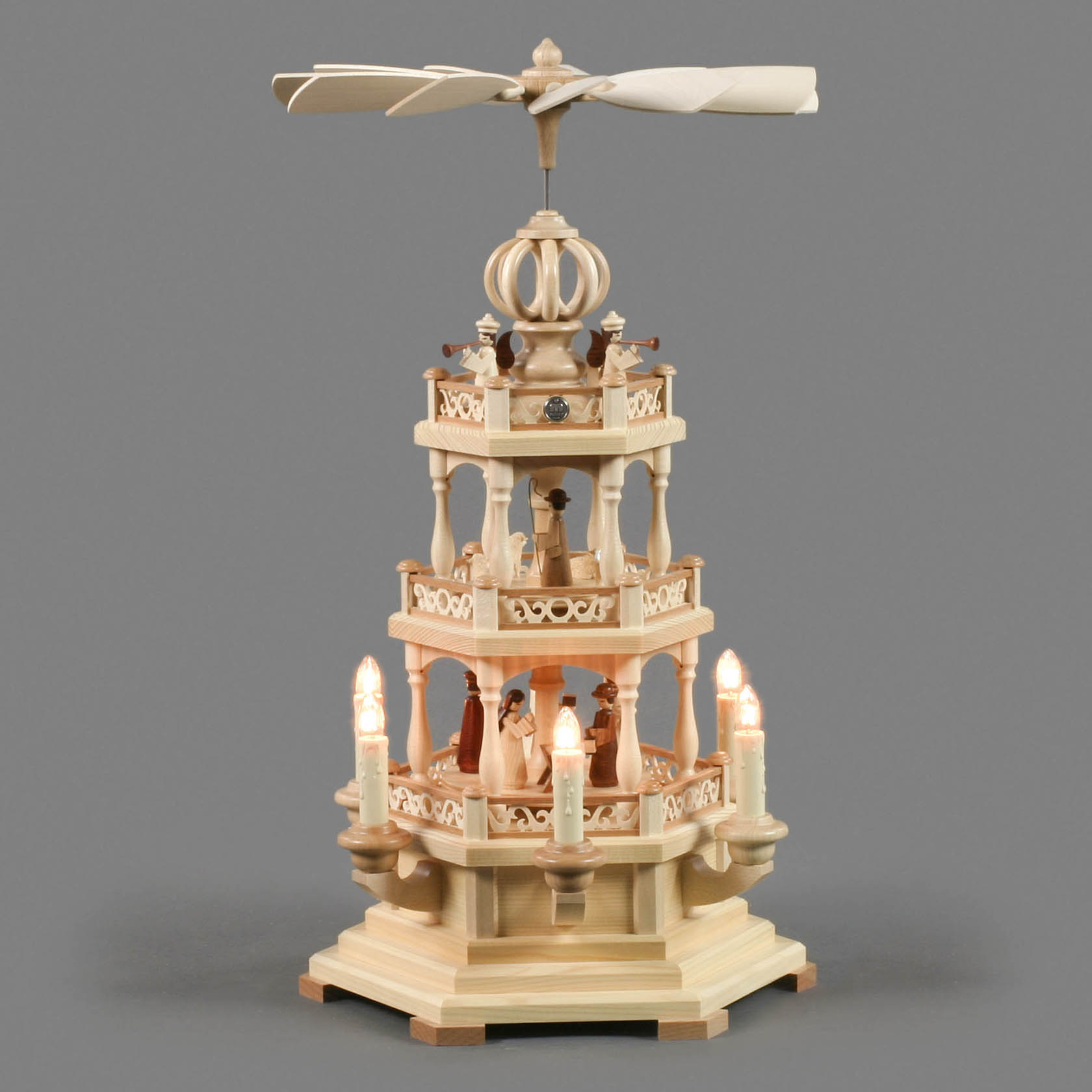 Zweistufige Weihnachtspyramide aus Holz mit Szenen der Geburt Christi. Elektrisches Licht beleuchtet die Ebenen; ein Propeller dreht sich oben.