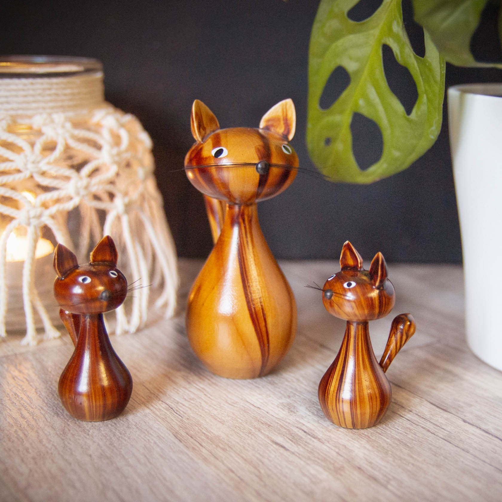 Drei geschnitzte Katzenfiguren aus Holz in verschiedenen Größen, die nebeneinander auf einem Tisch stehen.