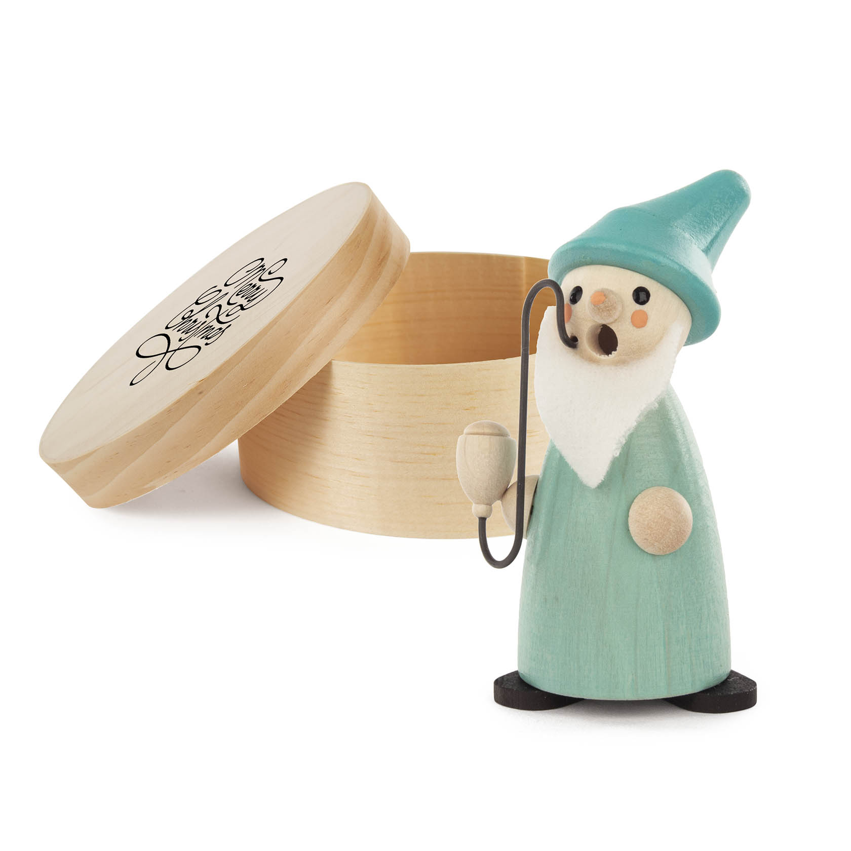 Holz-Wichtel in grünem Gewand und blauem Hut, hält eine Pfeife. Daneben eine offene runde Dose mit 'Merry Christmas' Motiv.