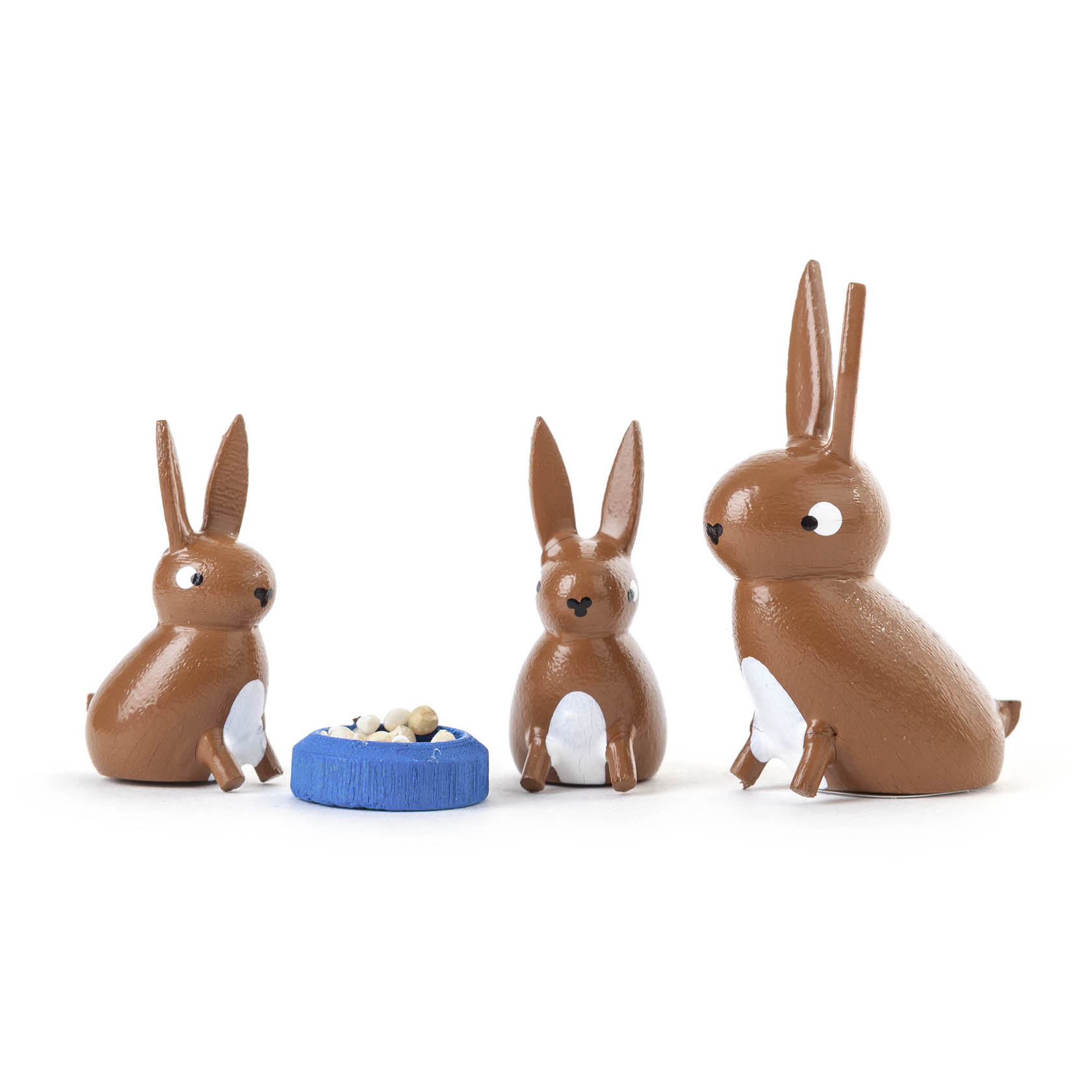 Drei braune Hasen aus Holz sitzen um einen blauen Teller mit weißen Kugeln. im Dregeno Online Shop günstig kaufen