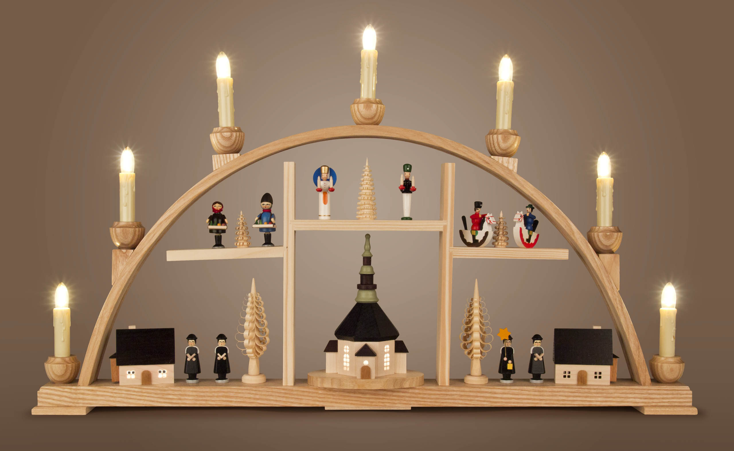 Ein Schwibbogen zeigt die Seiffener Kirche, Kurrende-Sänger und Erzgebirgsfiguren. Er ist elektrisch beleuchtet und aus Holz gefertigt.