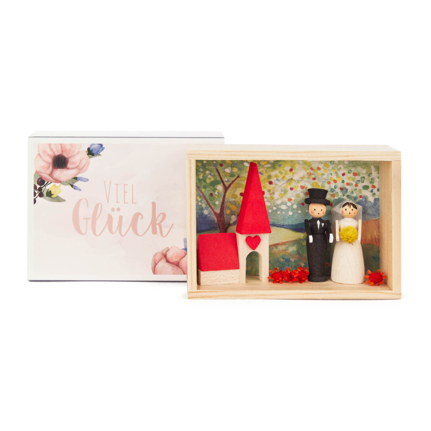 Holzkästchen mit Figuren eines Brautpaares und einem roten kleinen Haus, umgeben von roten Blättern. Im Hintergrund eine Landschaftsillustration. im Dregeno Online Shop günstig kaufen