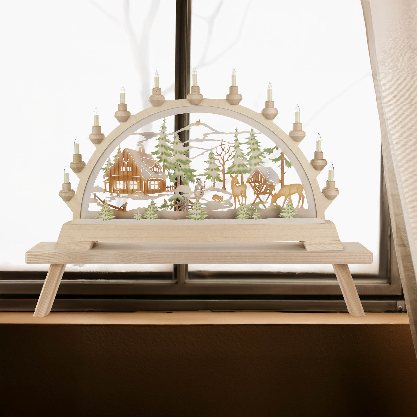 A wooden arched candle holder with colorful electric lighting, depicting a winter forest scene with a cabin and wildlife.
