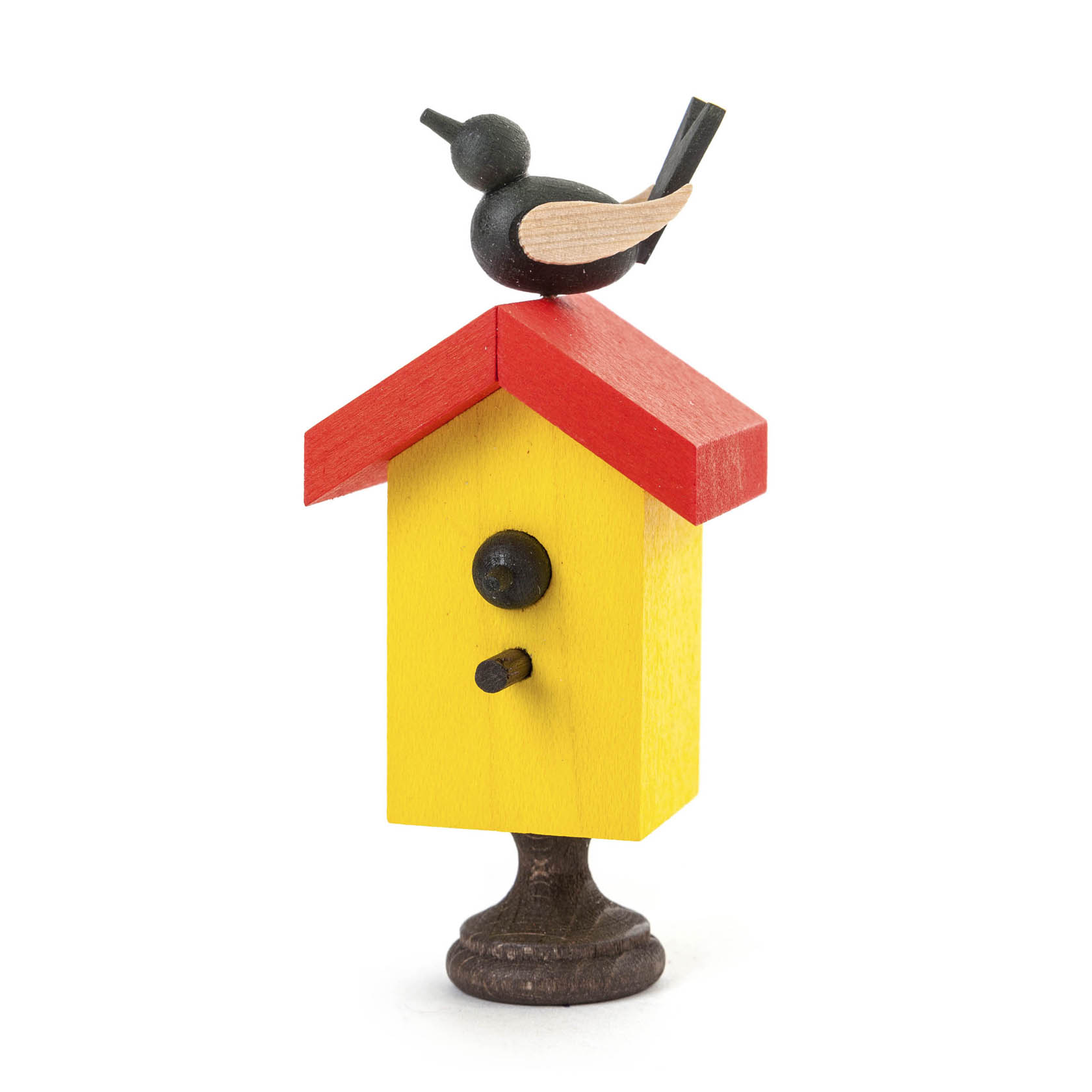 Ein bunt bemaltes Starhaus mit rotem Dach und gelber Fassade. Auf dem Dach sitzt ein minimalistischer Singvogel aus Holz mit schwarzem Körper und hellem Schnabel. im Dregeno Online Shop günstig kaufen