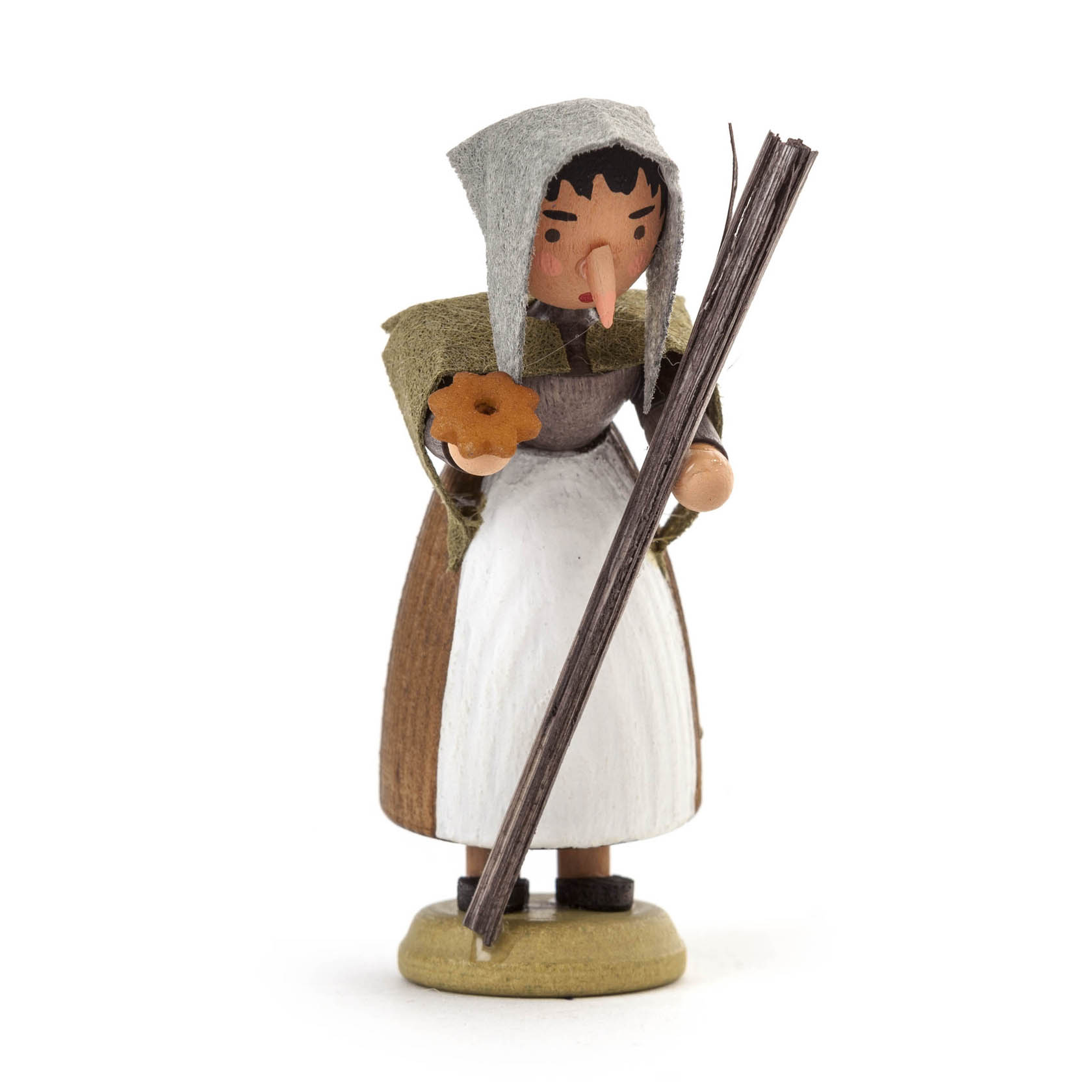 Figur einer traditionellen Hexe mit spitzer Nase, haarigem Besen, grauem Umhang und weißer Schürze, hält einen orangefarbenen Keks in der Hand. im Dregeno Online Shop günstig kaufen