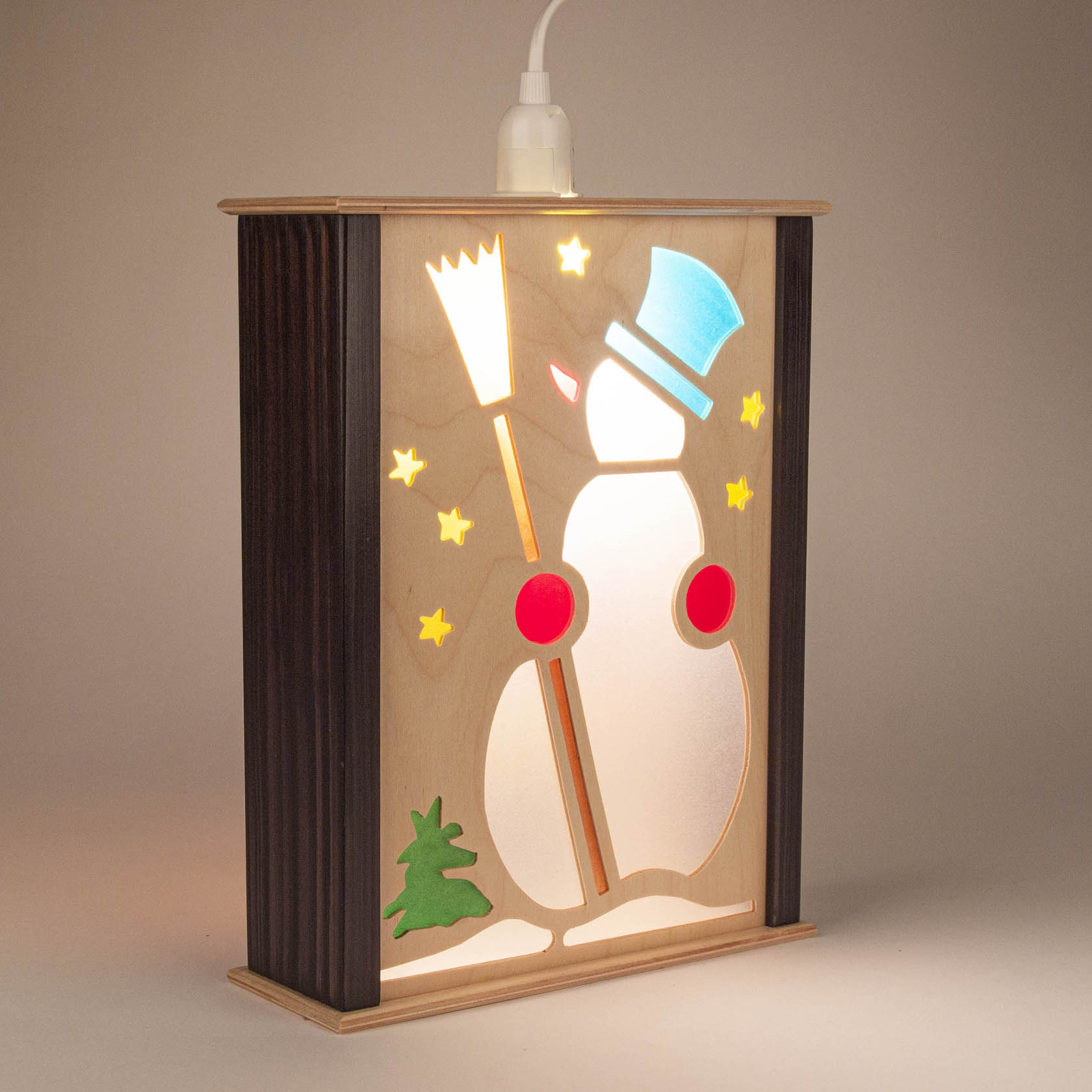 Wooden window lantern depicting a festive snowman with top hat holding a broom, glowing light inside, surrounded by stars and a small green tree.