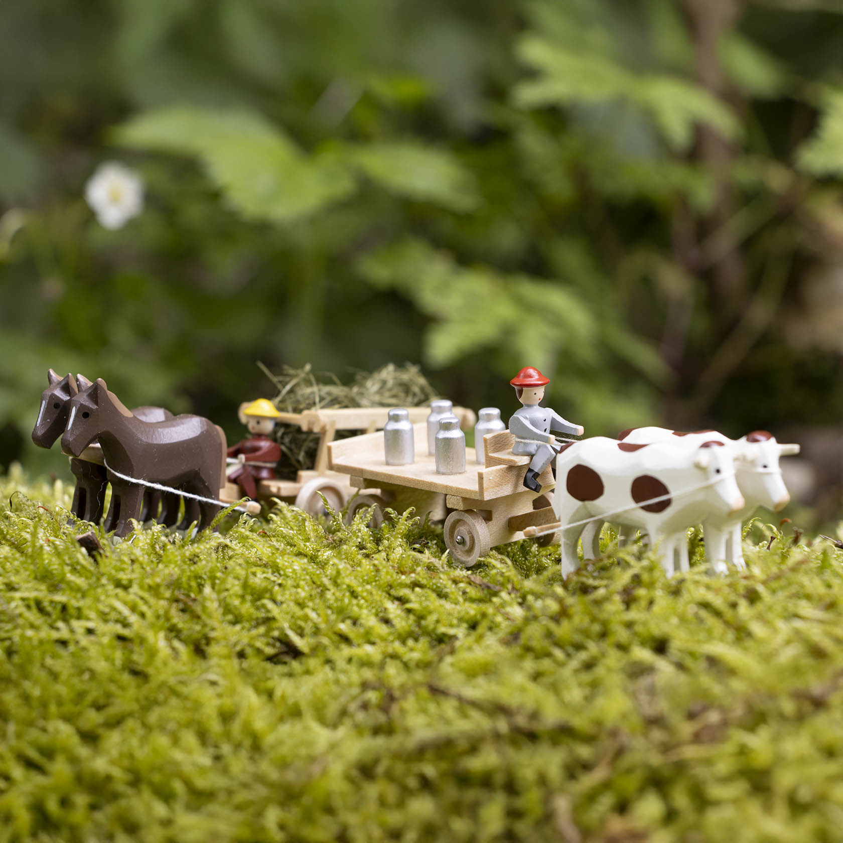 Miniatur eines Gespanns mit zwei Pferden, die einen Leiterwagen mit Milchkannen ziehen, darauf ist Heu. Dahinter steht ein Bauer neben zwei Kühen.