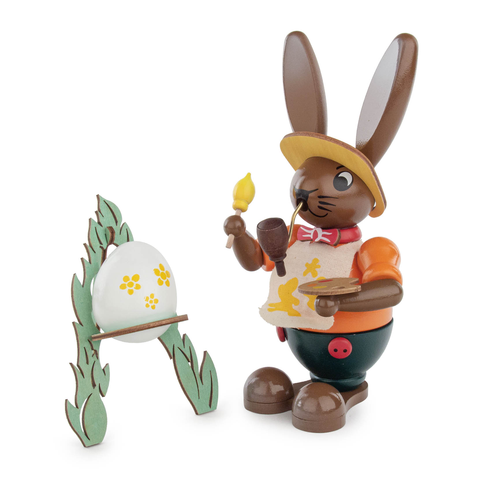 Ein Räucherhase mit gelber Malschürze, der ein Pinsel hält und vor einer Staffelei mit einem bemalten Ei steht. im Dregeno Online Shop günstig kaufen