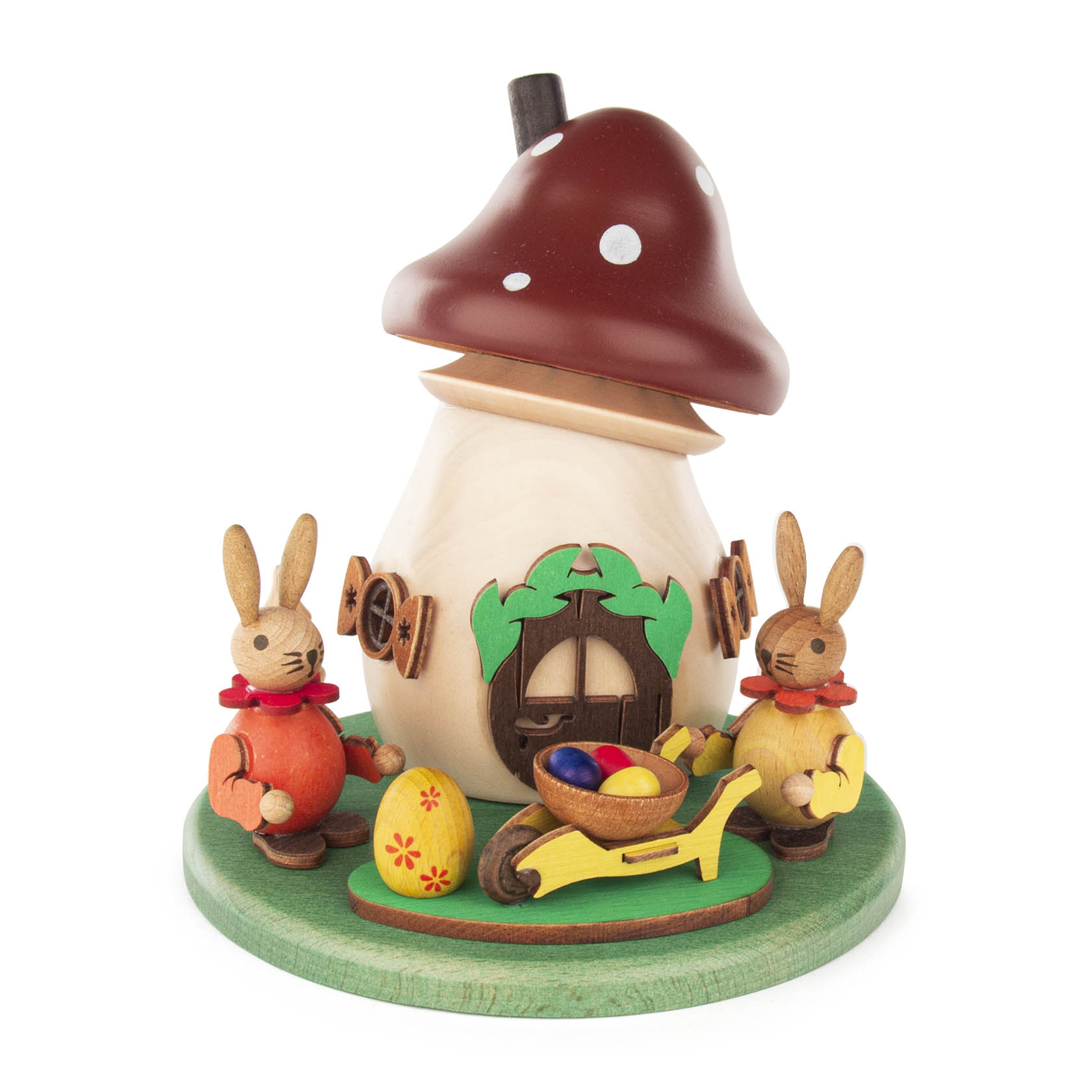 Ein dekorativer Räucherpilz aus Holz mit einem braunen Dach und weißen Punkten. Zwei Osterhasen mit süßen Accessoires sitzen daneben. Ein Rad mit bunten Ostereiern ist im Vordergrund. im Dregeno Online Shop günstig kaufen