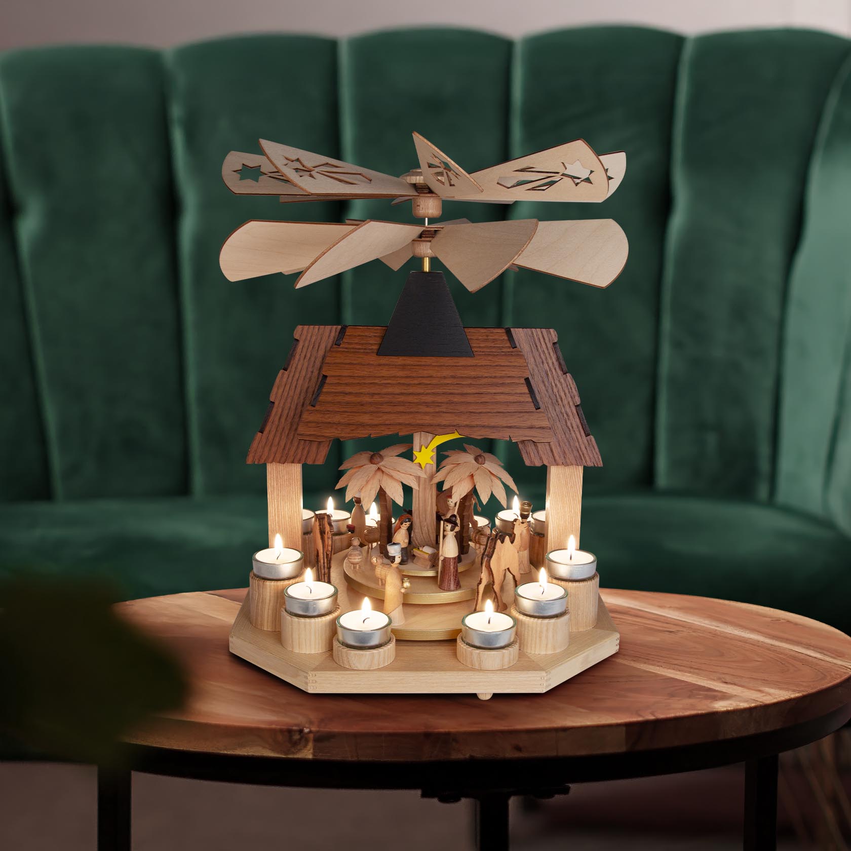 Holzpyramide mit Christi Geburt und Teelichtern, bestehend aus zwei Etagen, mit zwei Flügelrädern und einer Spitze, auf einem Tisch stehend.