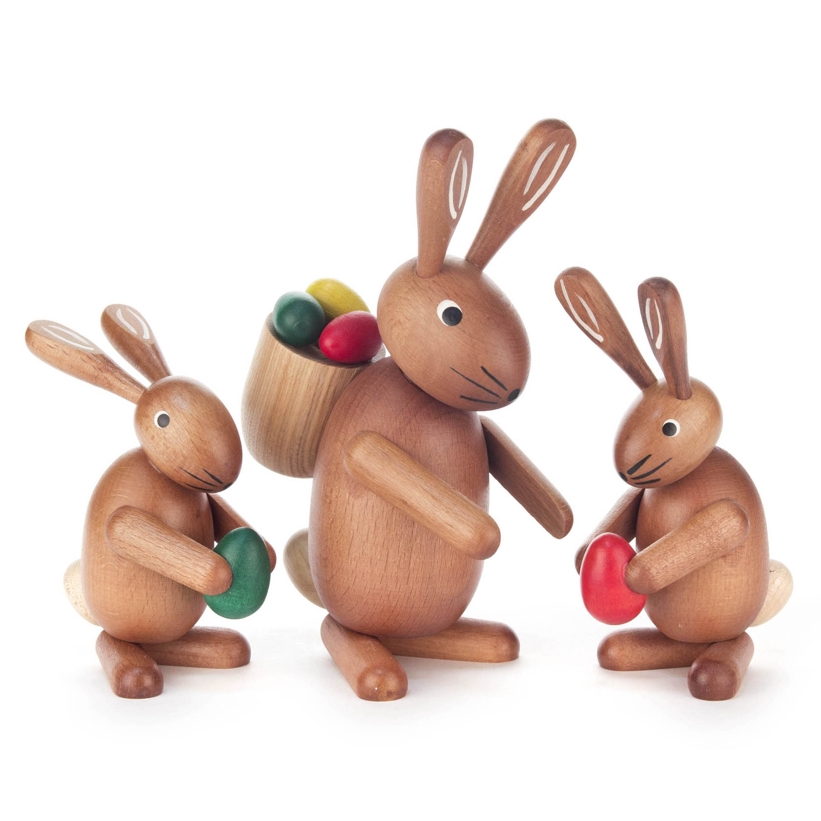 Drei hölzerne Hasenfiguren, die Eier halten. Der mittlere Hase hat eine Tasche mit mehrfarbigen Eiern auf dem Rücken. im Dregeno Online Shop günstig kaufen