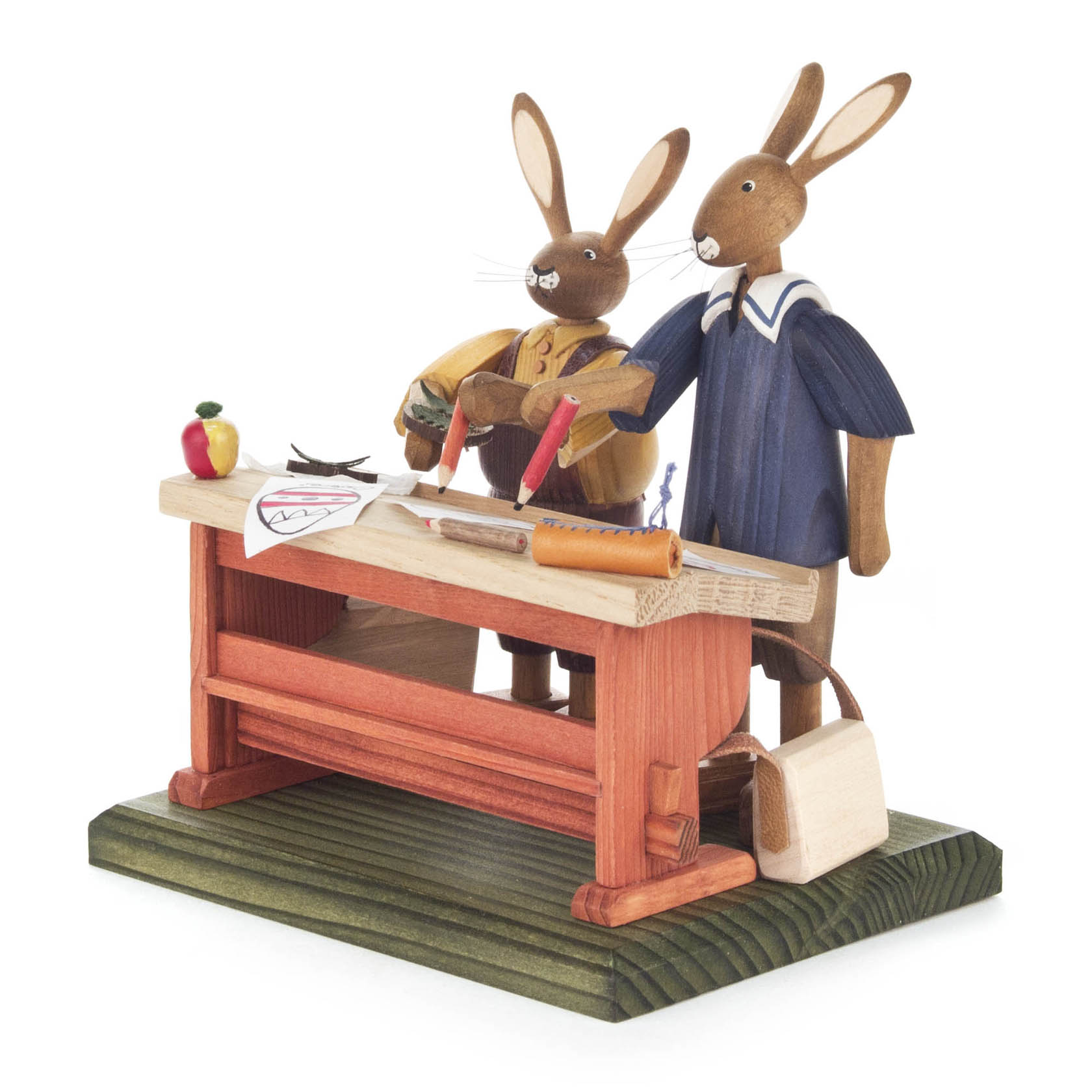 Zwei Hasenfiguren in traditioneller Kleidung stehen an einer Schulbank. Einer schreibt, der andere beobachtet. Auf dem Tisch liegen Schulmaterialien. im Dregeno Online Shop günstig kaufen